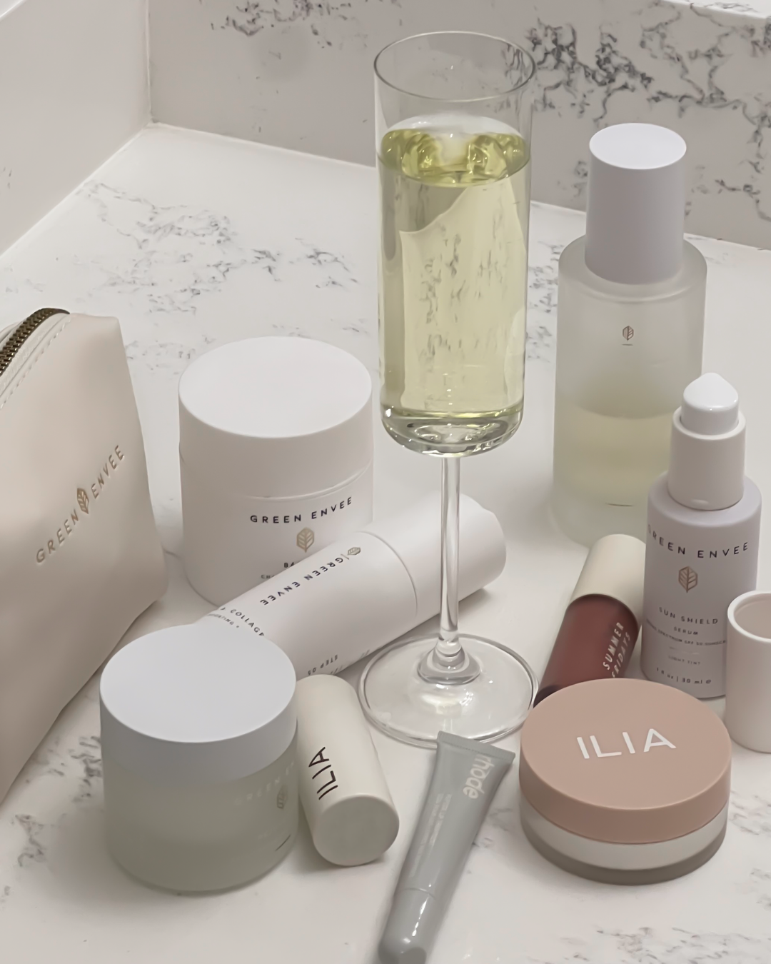 Collection of skincare and beauty products, including creams, serums, and a glass of white wine on a marble countertop.