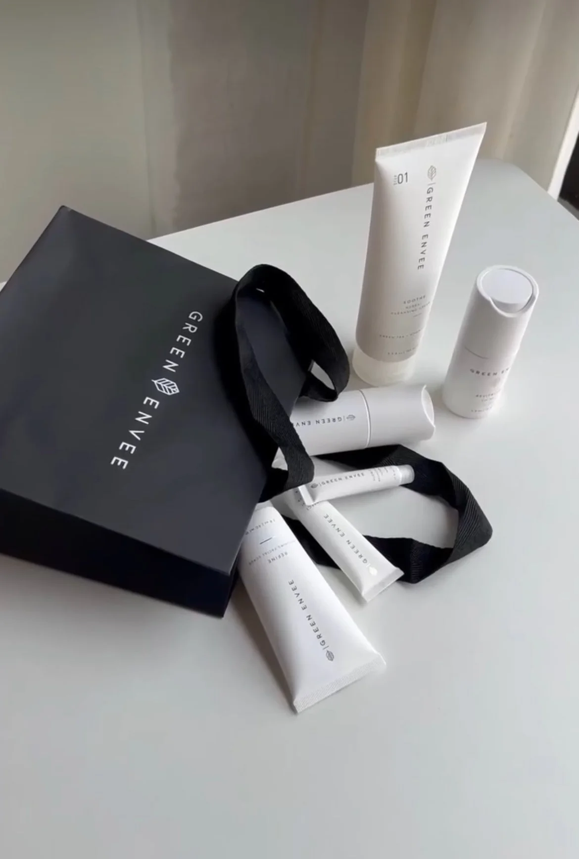 Skincare products placed on a white surface with a black tote bag displaying the Green Envee logo.