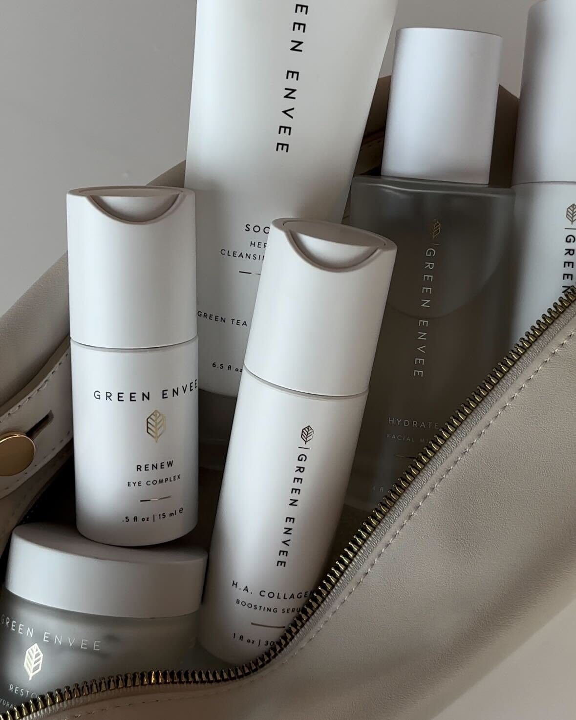 A collection of Green Envee skincare products, including eye cream, collagen boosting serum, and facial cleanser inside a beige bag with a gold zipper.
