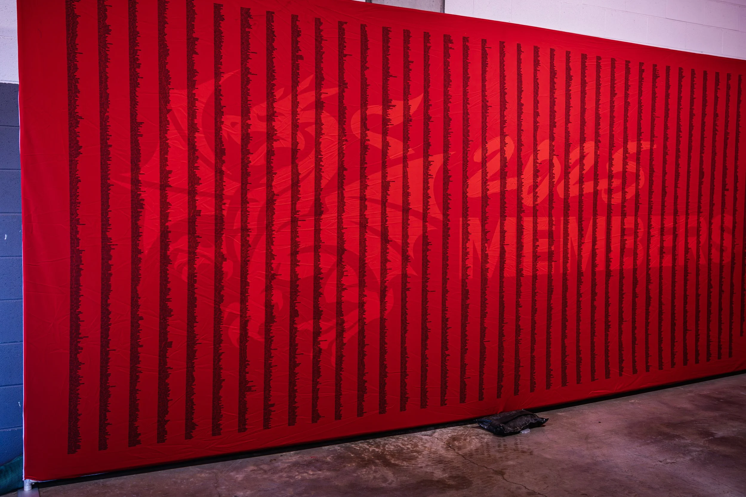 Red wall with black text and a faint emblem, installed indoors on a concrete floor.