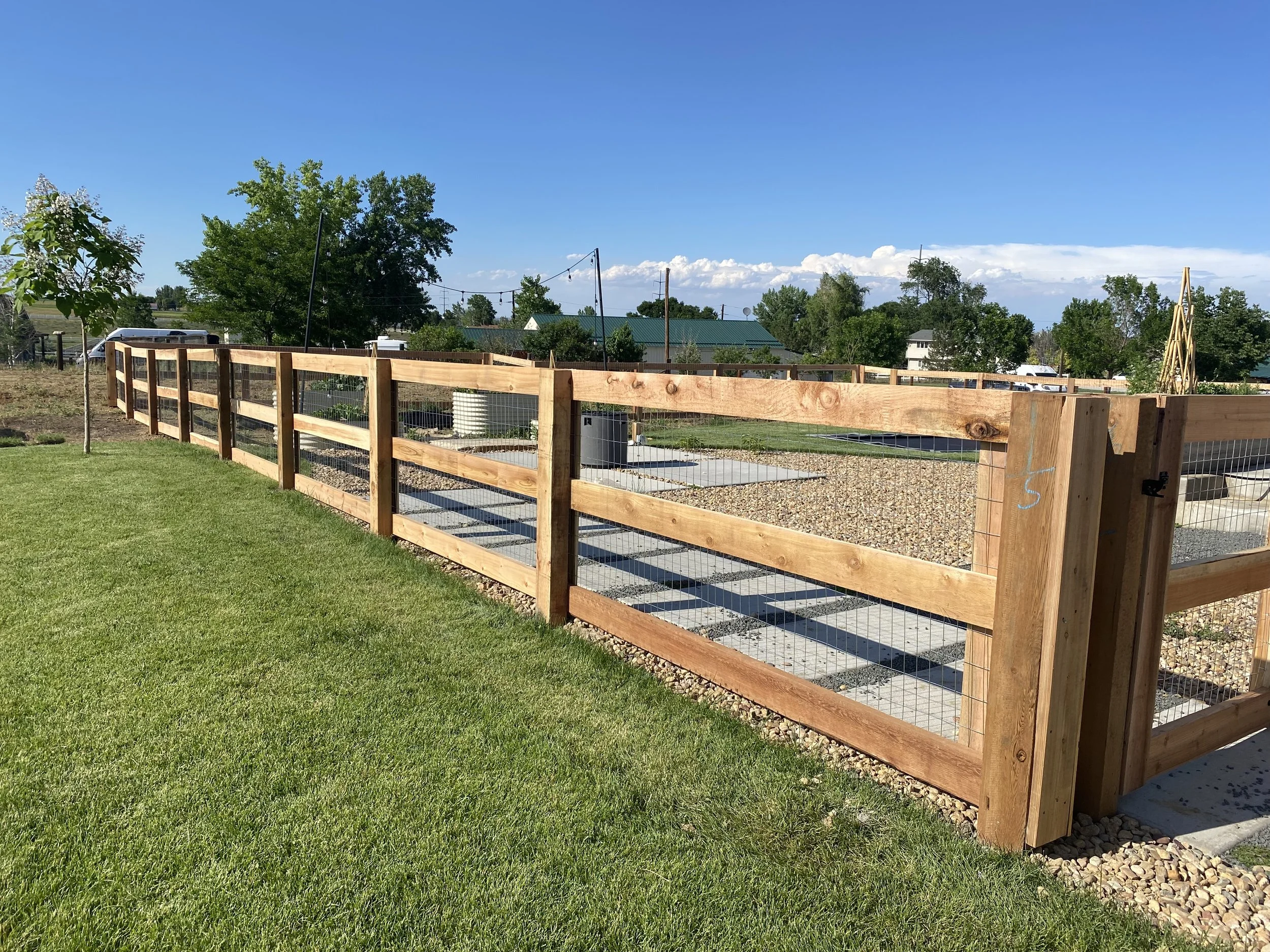Newly built wooden and wire fence separating a grassy yard from a garden with gravel paths and garden beds.