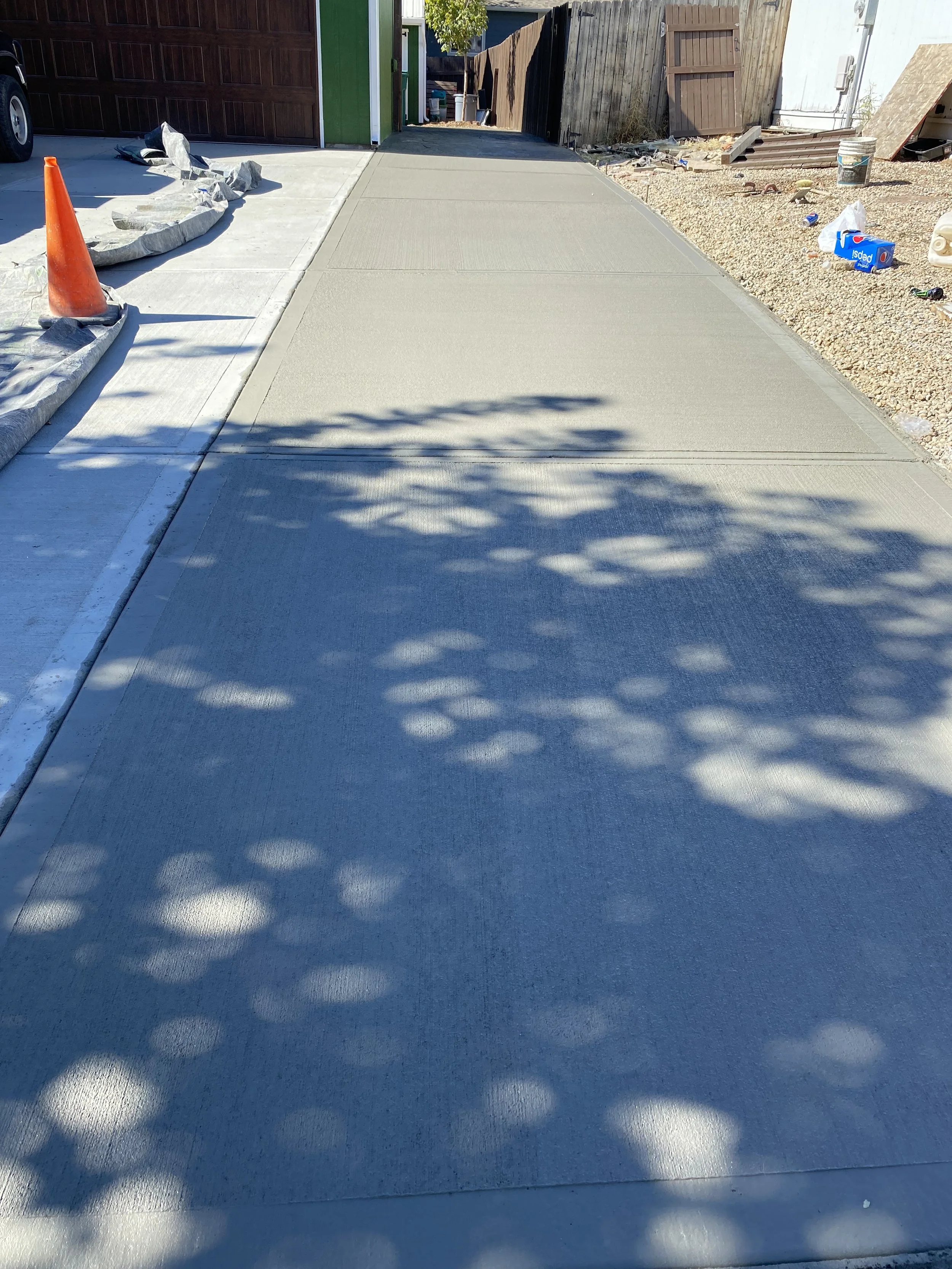 Newly poured concrete sidewalk next to a garage with construction materials and tools nearby.