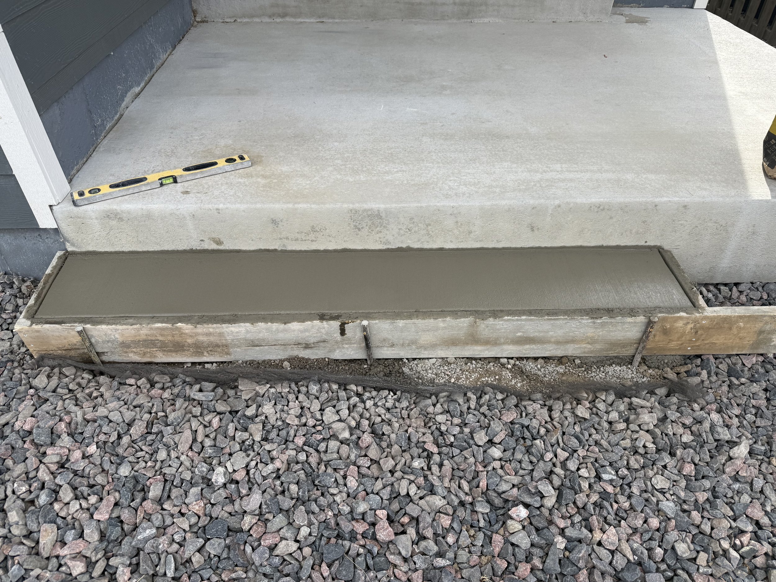 Concrete step with freshly poured concrete, a level tool on top, and gravel surrounding the area.