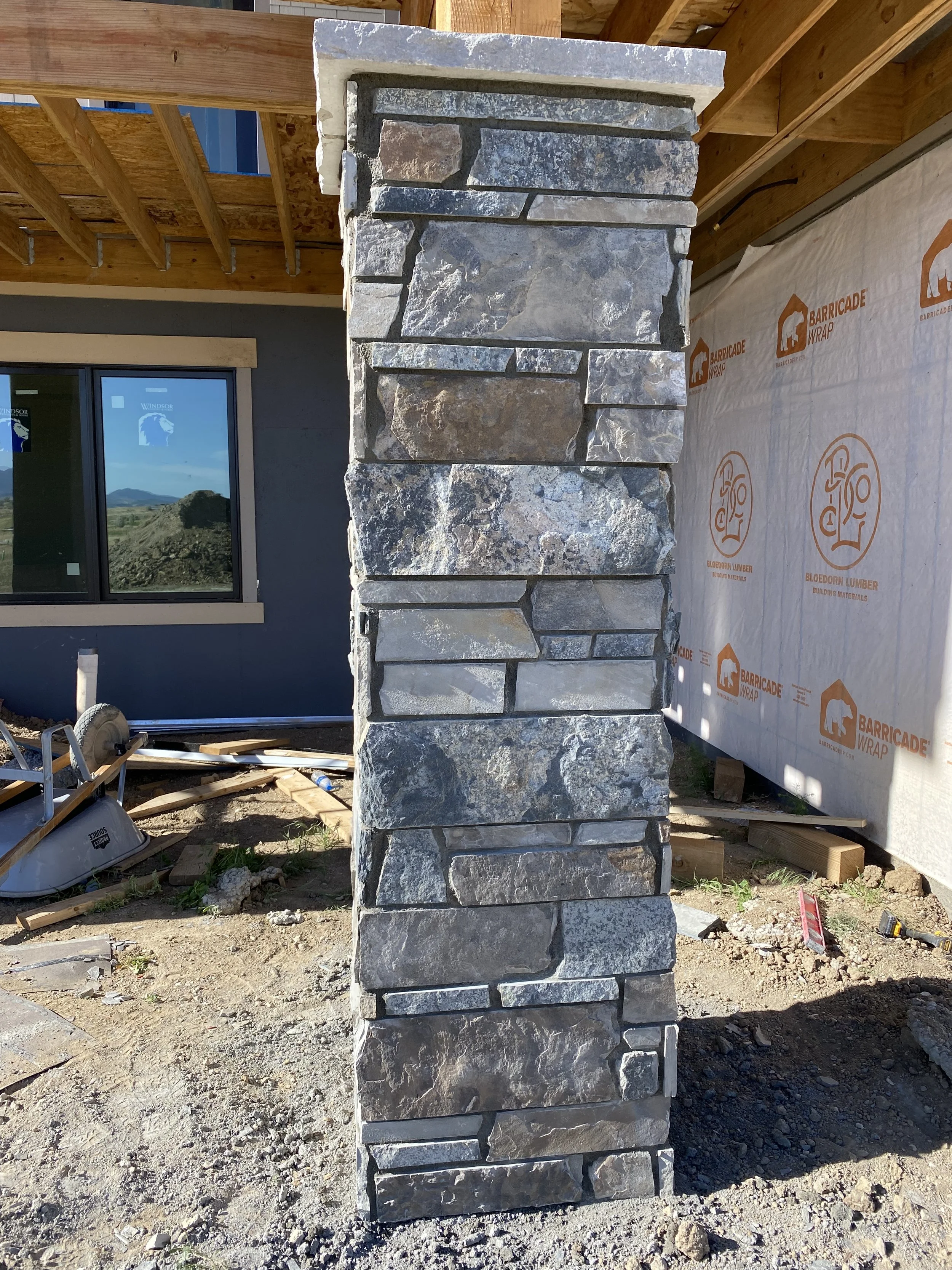 A stone pillar under construction on a construction site with a partially built house in the background.