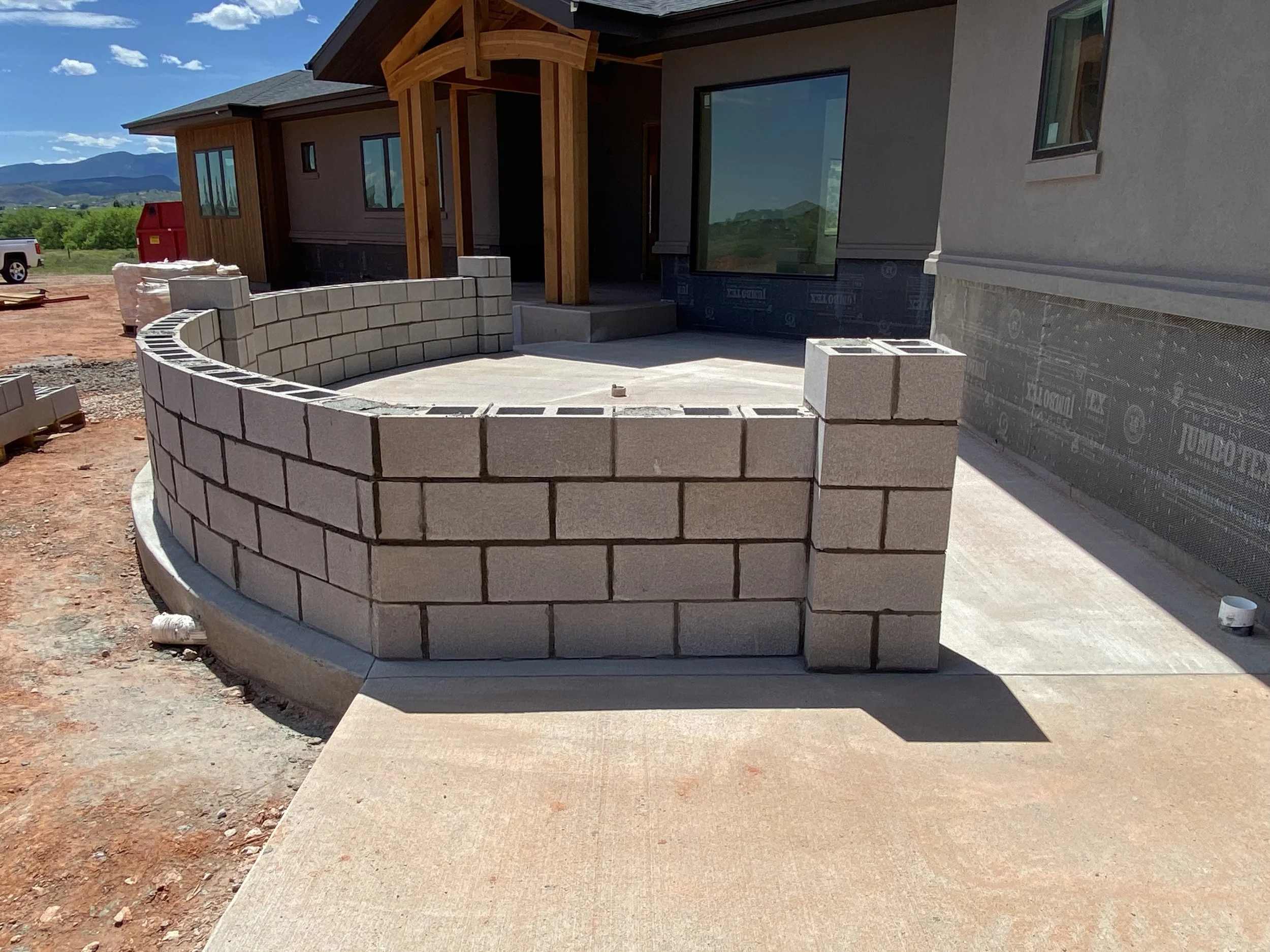 Construction site of a house with a curved brick wall partially built around a concrete porch area.