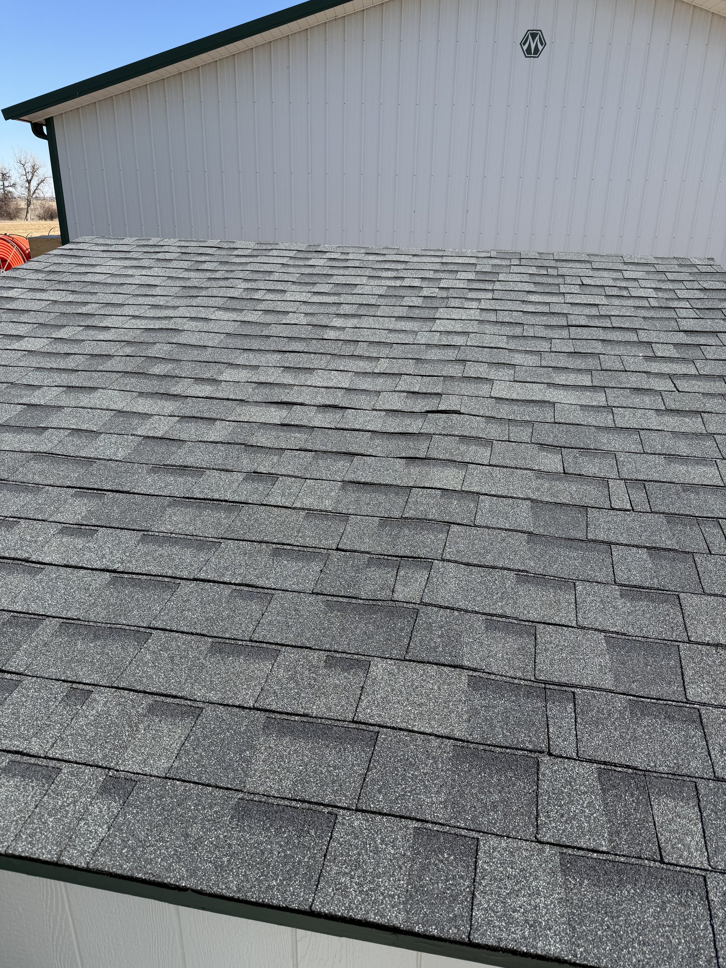 Close-up of asphalt shingle roof on a building with a white metal wall and a green trim