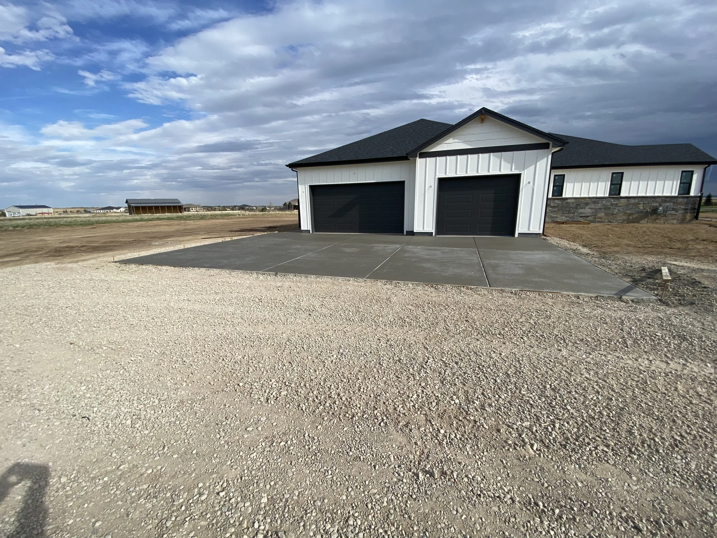 Newly constructed house with a black garage door, white siding, and a concrete driveway in a rural area.