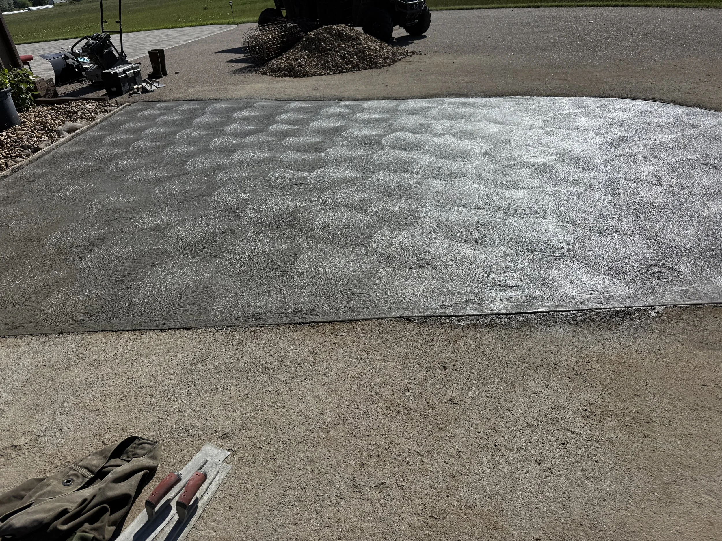 A freshly poured concrete slab with a decorative swirl pattern, surrounded by construction tools and materials, on a construction site.