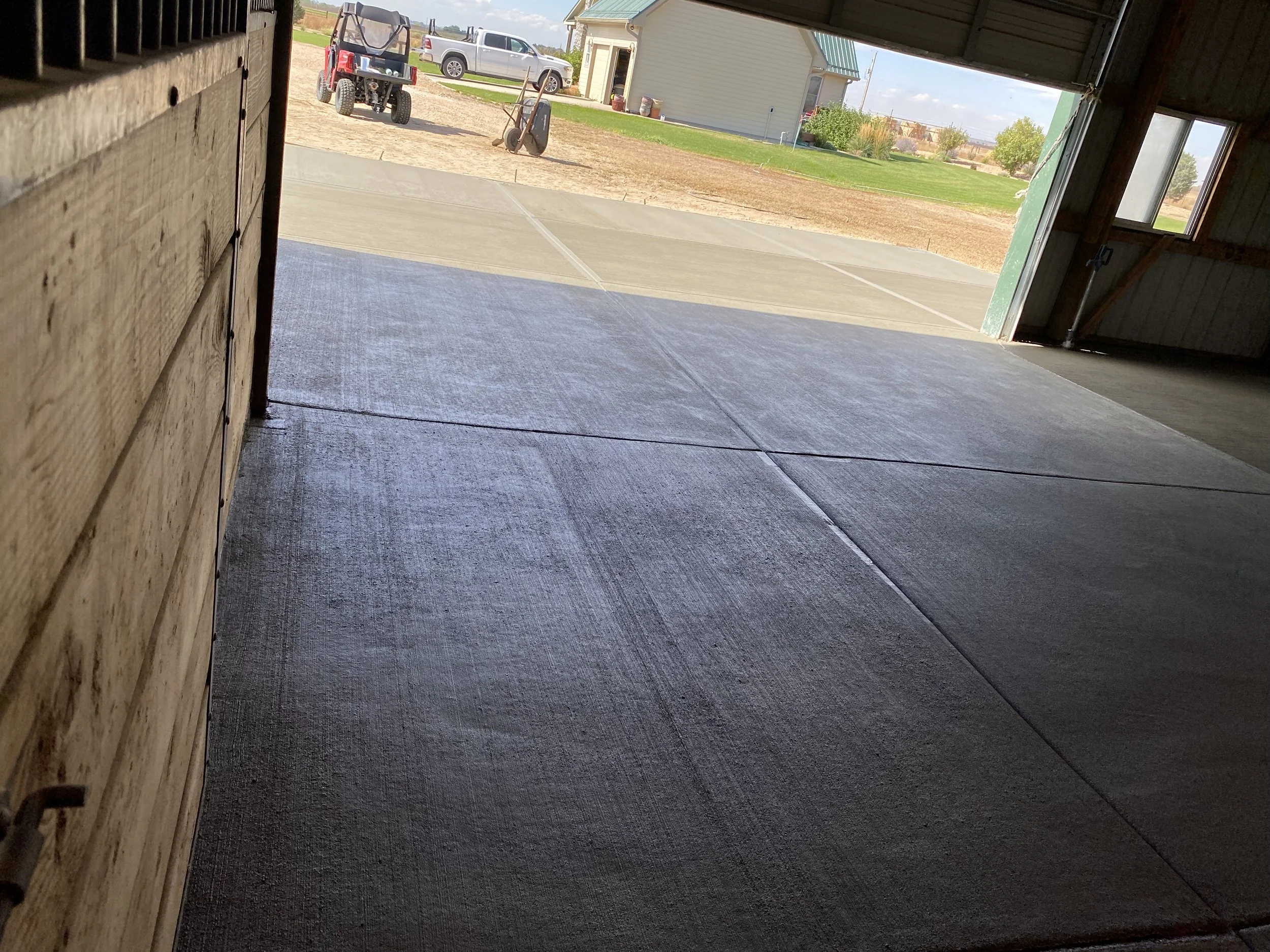 View from inside a garage looking out onto a driveway with a stroller and parked vehicles, with a house, lawn, and trees in the background.
