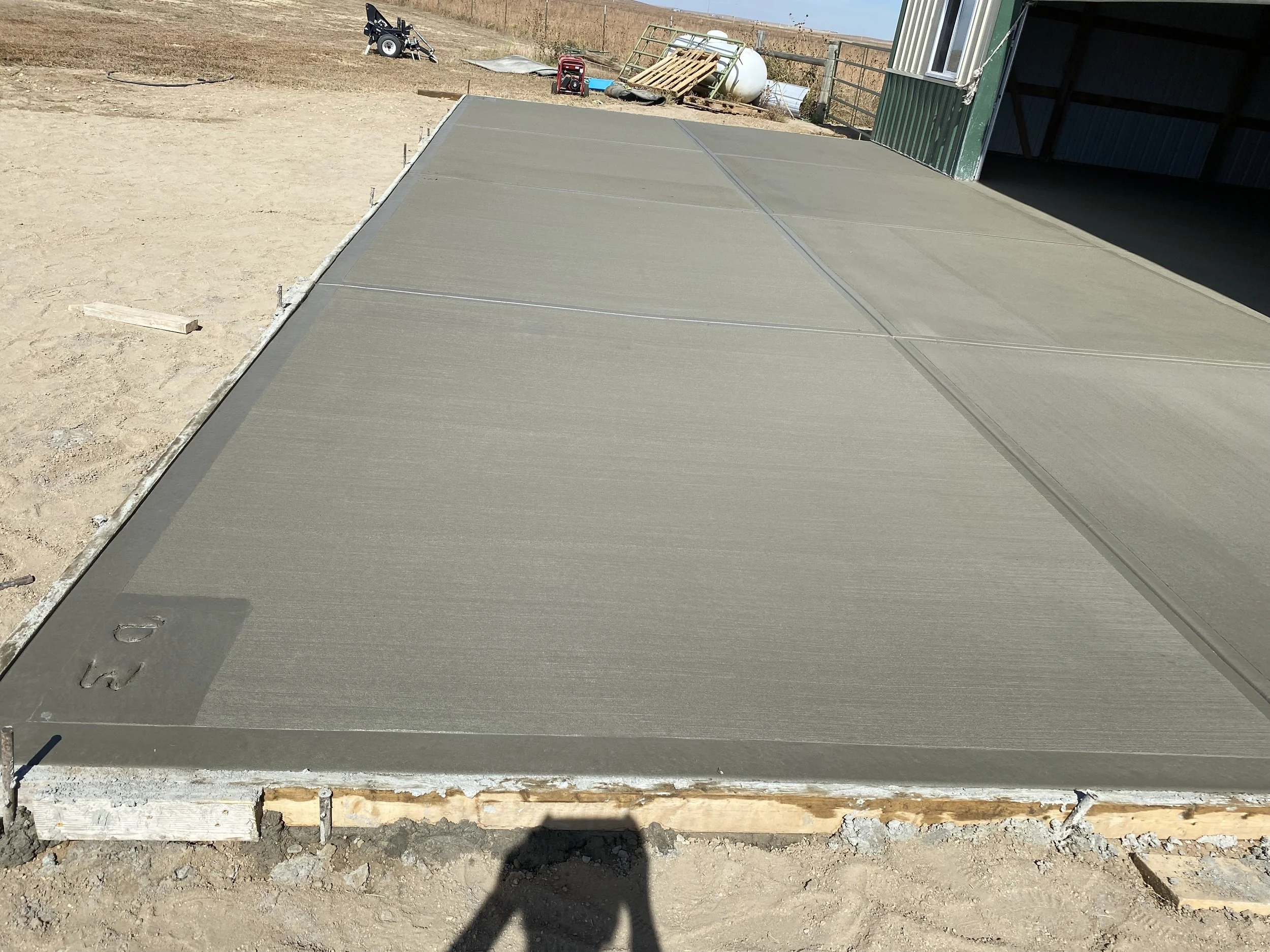Freshly poured concrete slab at a construction site, with some construction tools and materials in the background.