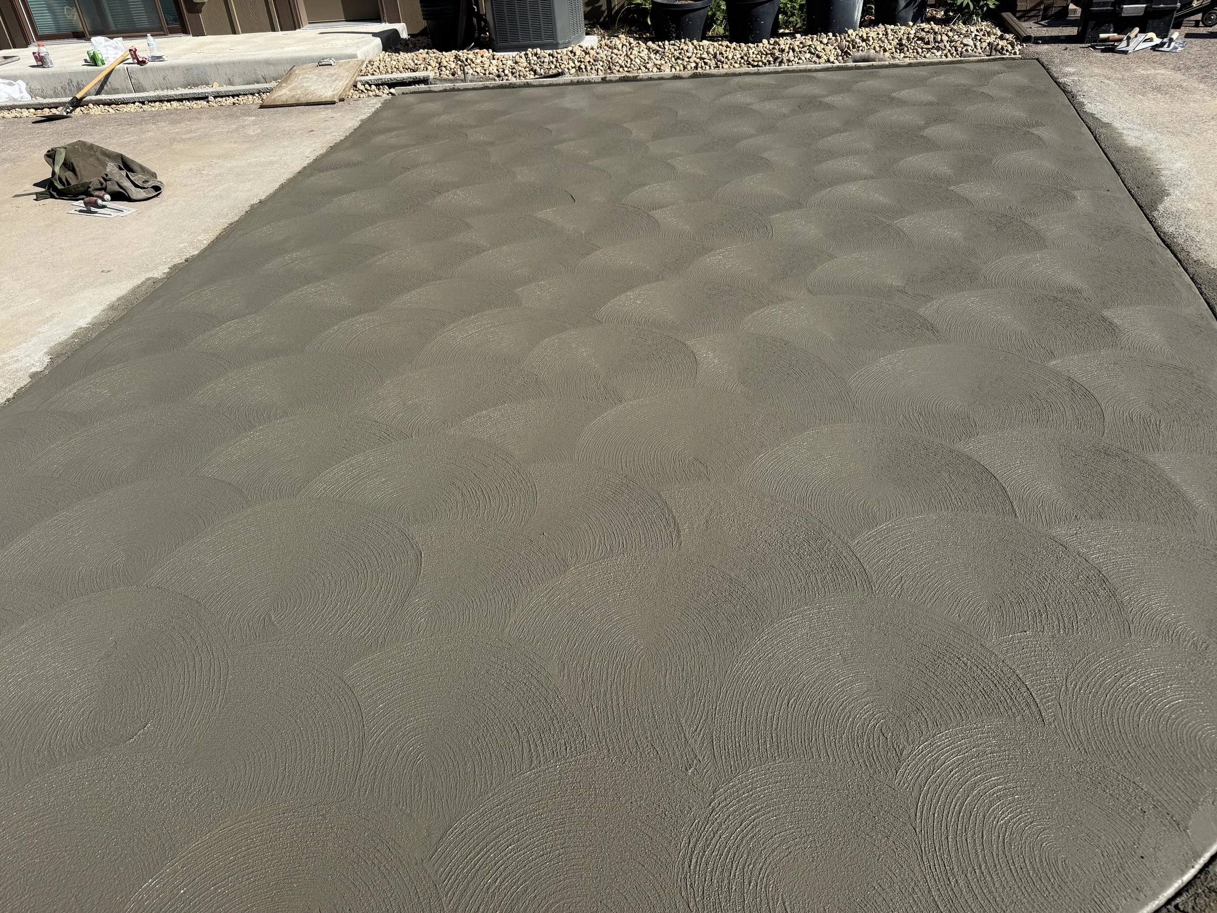 Freshly poured concrete with a textured swirl pattern on a driveway or sidewalk construction site.
