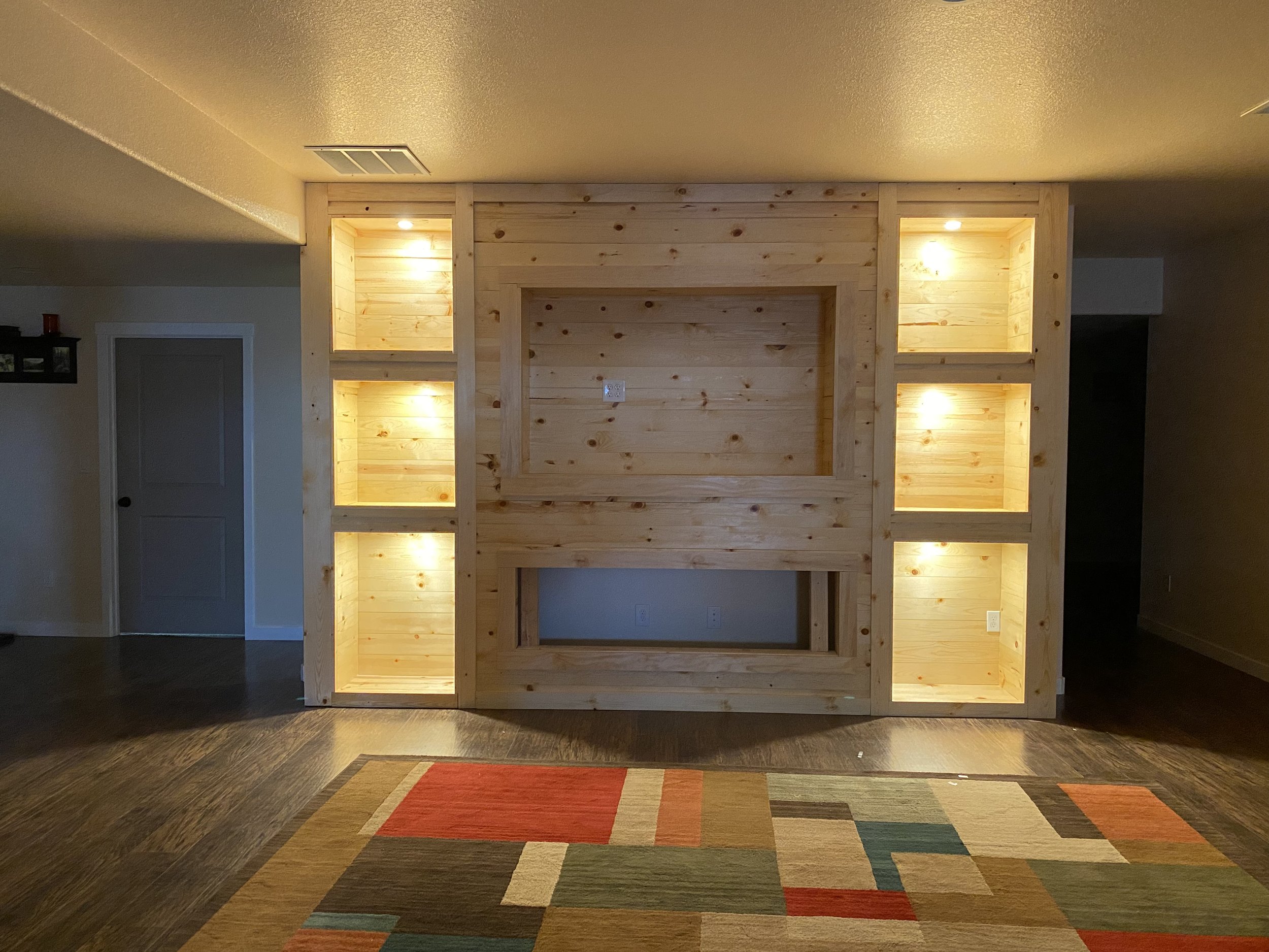 Wood-paneled entertainment wall with built-in shelves and recessed lighting in a living room.
