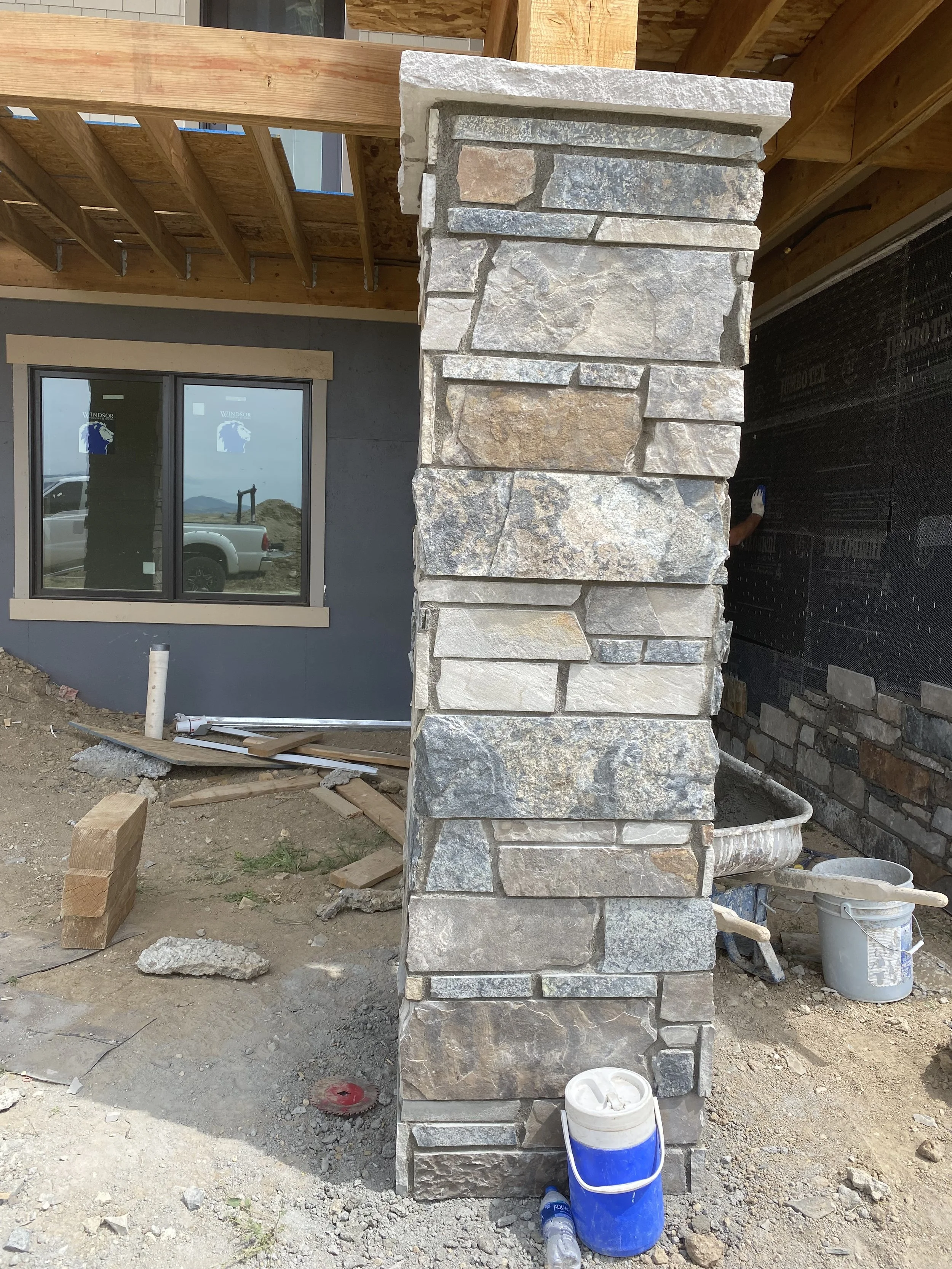 Close-up of a stone and brick exterior wall of a building under construction, with construction tools, a bucket, and a water bottle on the ground nearby.