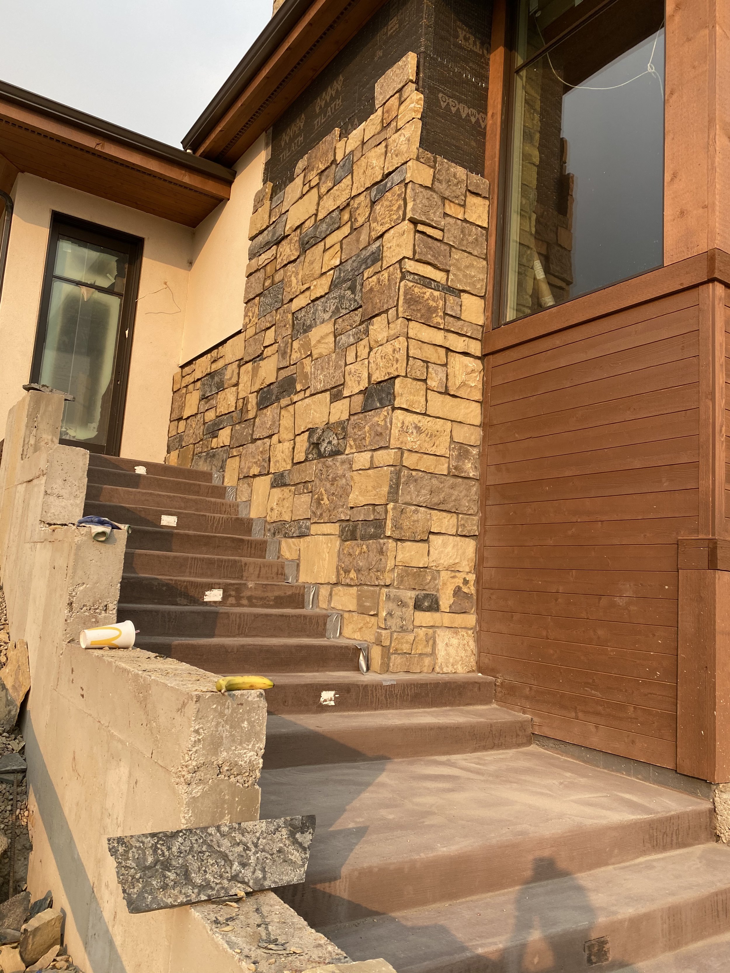 Construction of exterior stairs and wall with stone and wood paneling on a house. Tools and construction materials are present on the stairs.