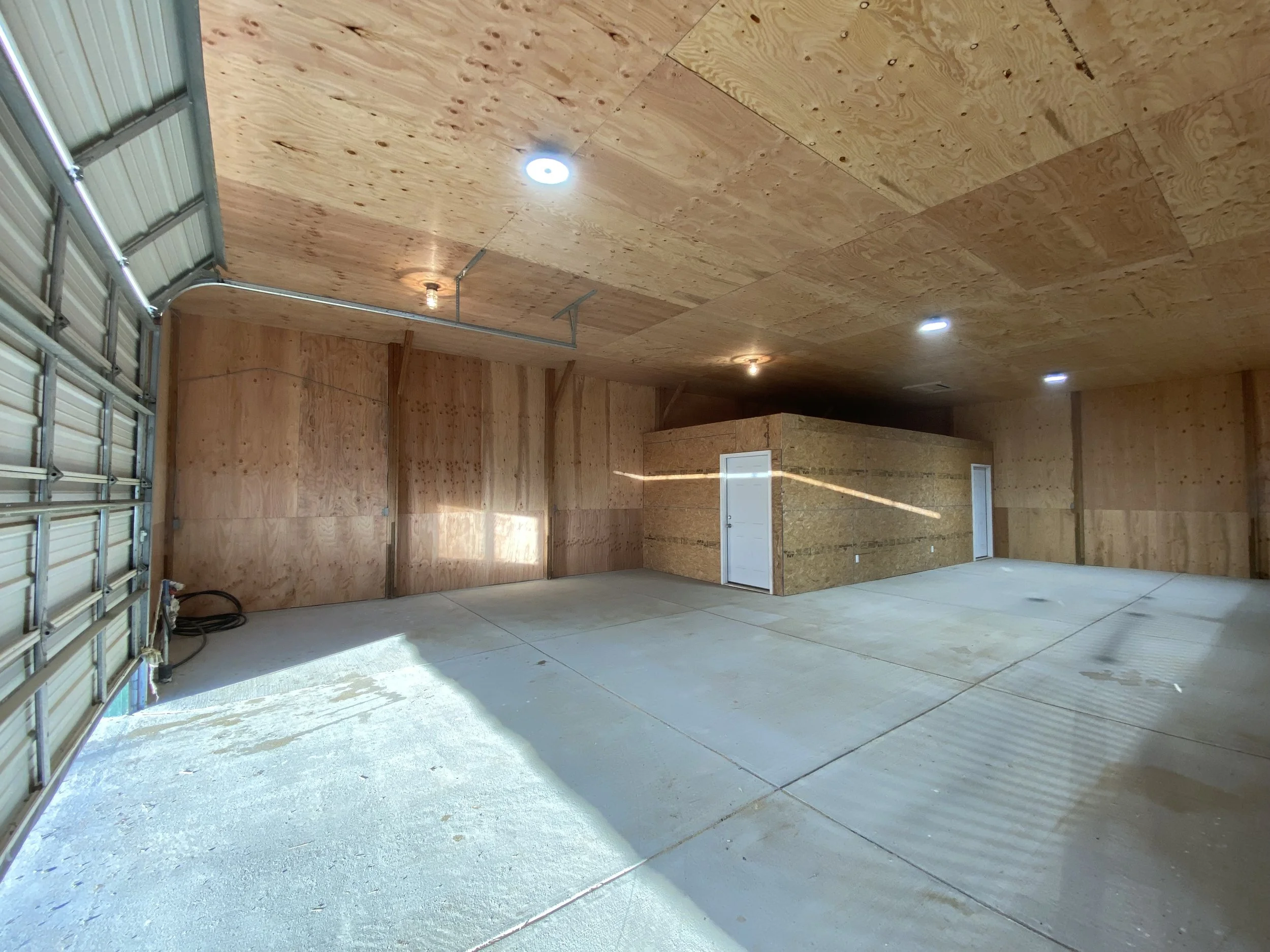 Empty garage with unfinished wooden walls and ceiling, concrete floor, and a partially open garage door.