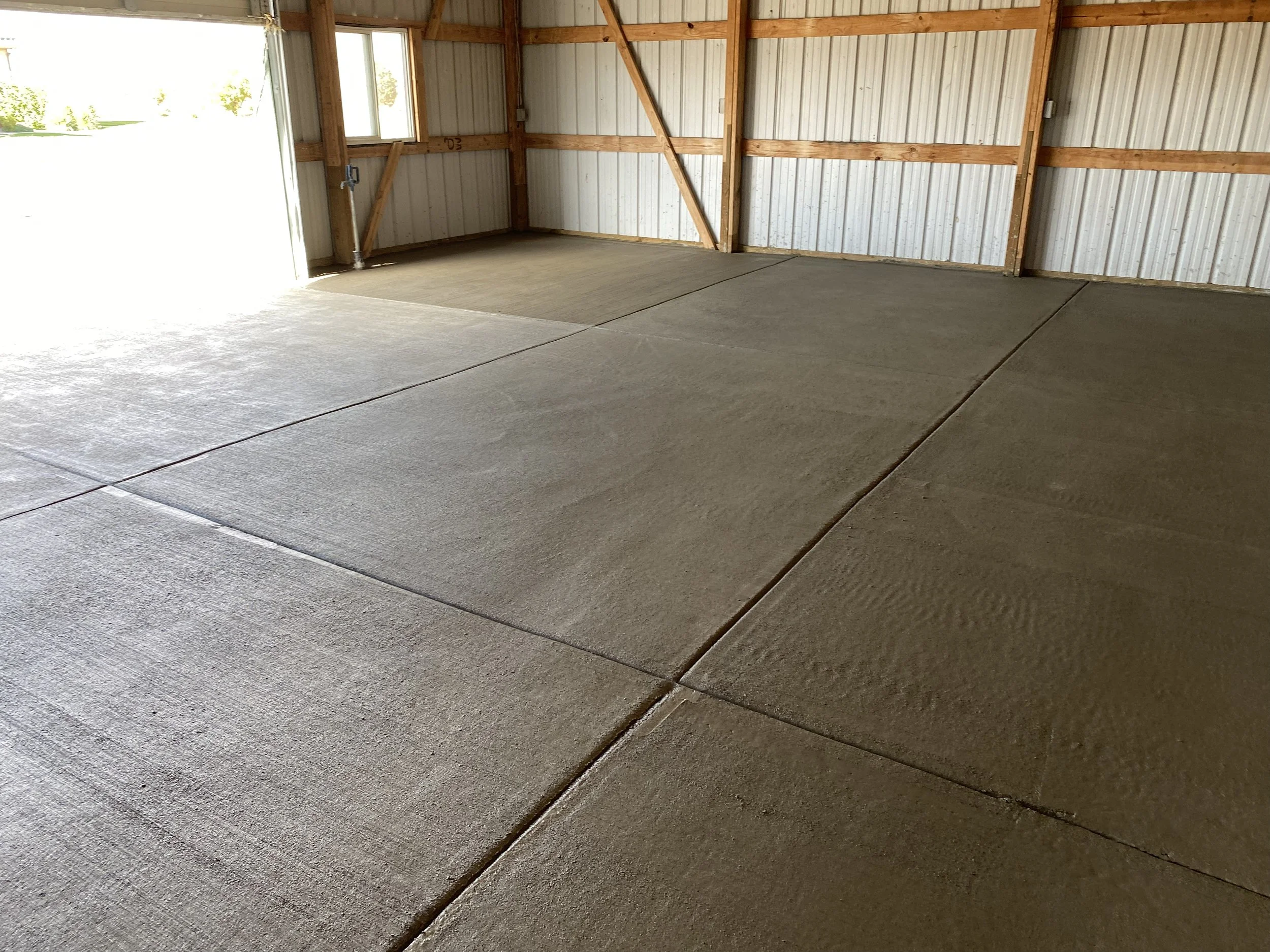 Empty garage with concrete floor and metal wall panels, wooden framing, and a partially open garage door