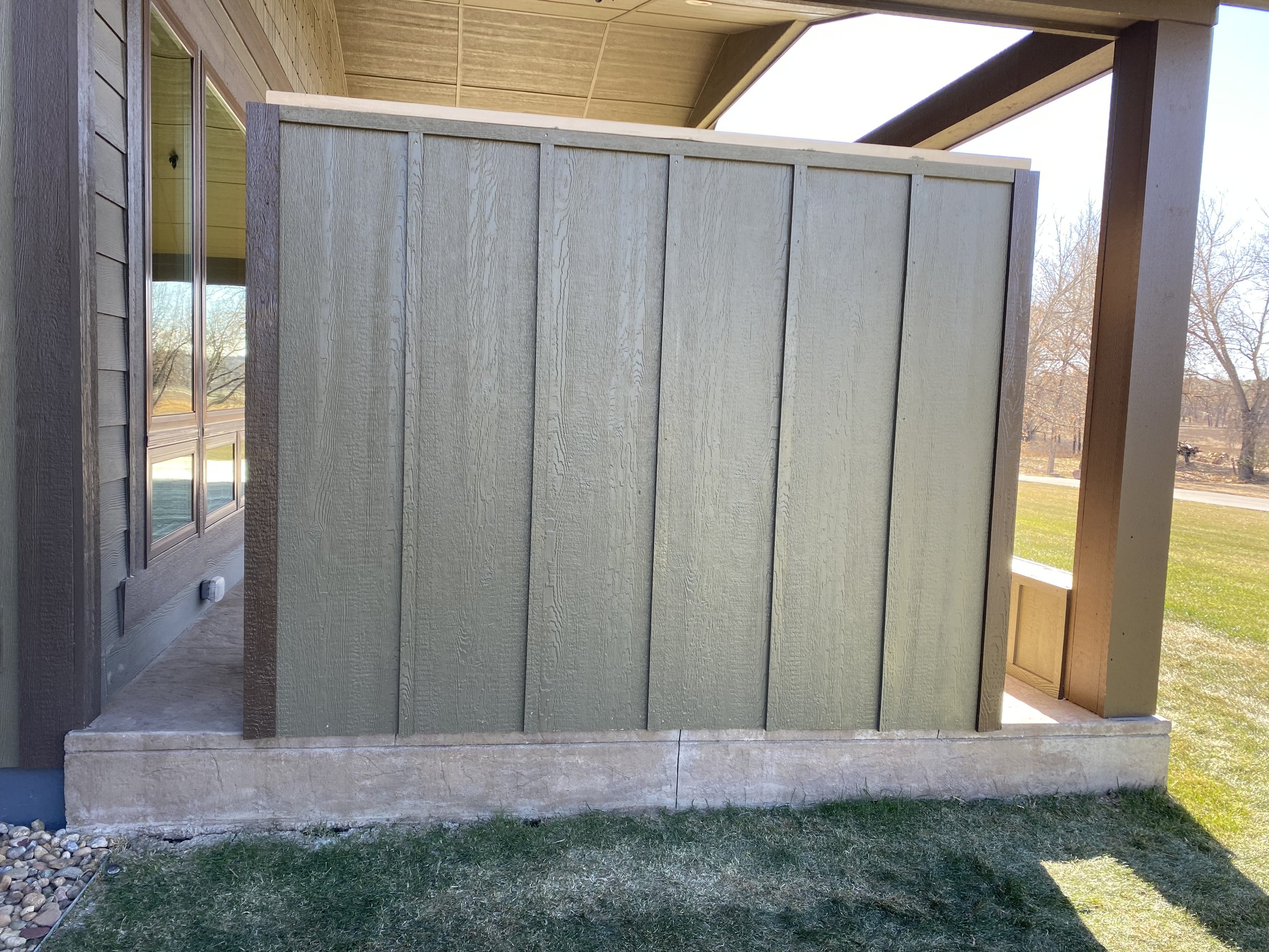 Outdoor privacy panel or fence near a house, with grass and trees in the background.