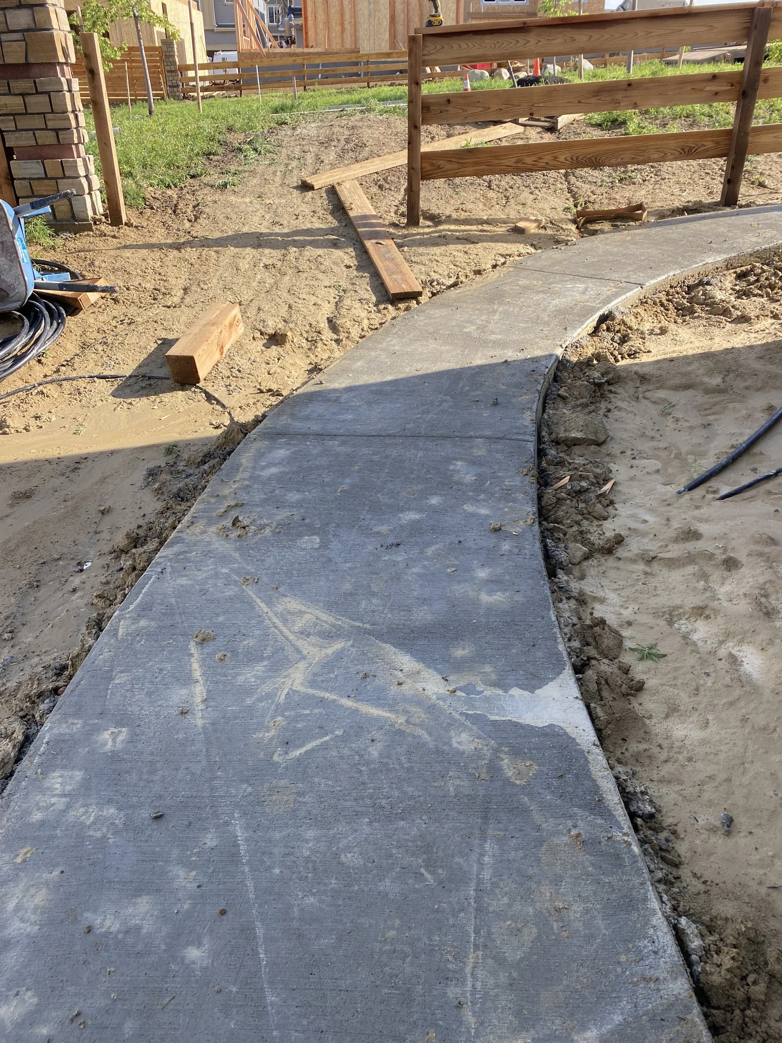 Newly poured concrete pathway with curved design under construction, with wooden formwork and construction tools nearby.