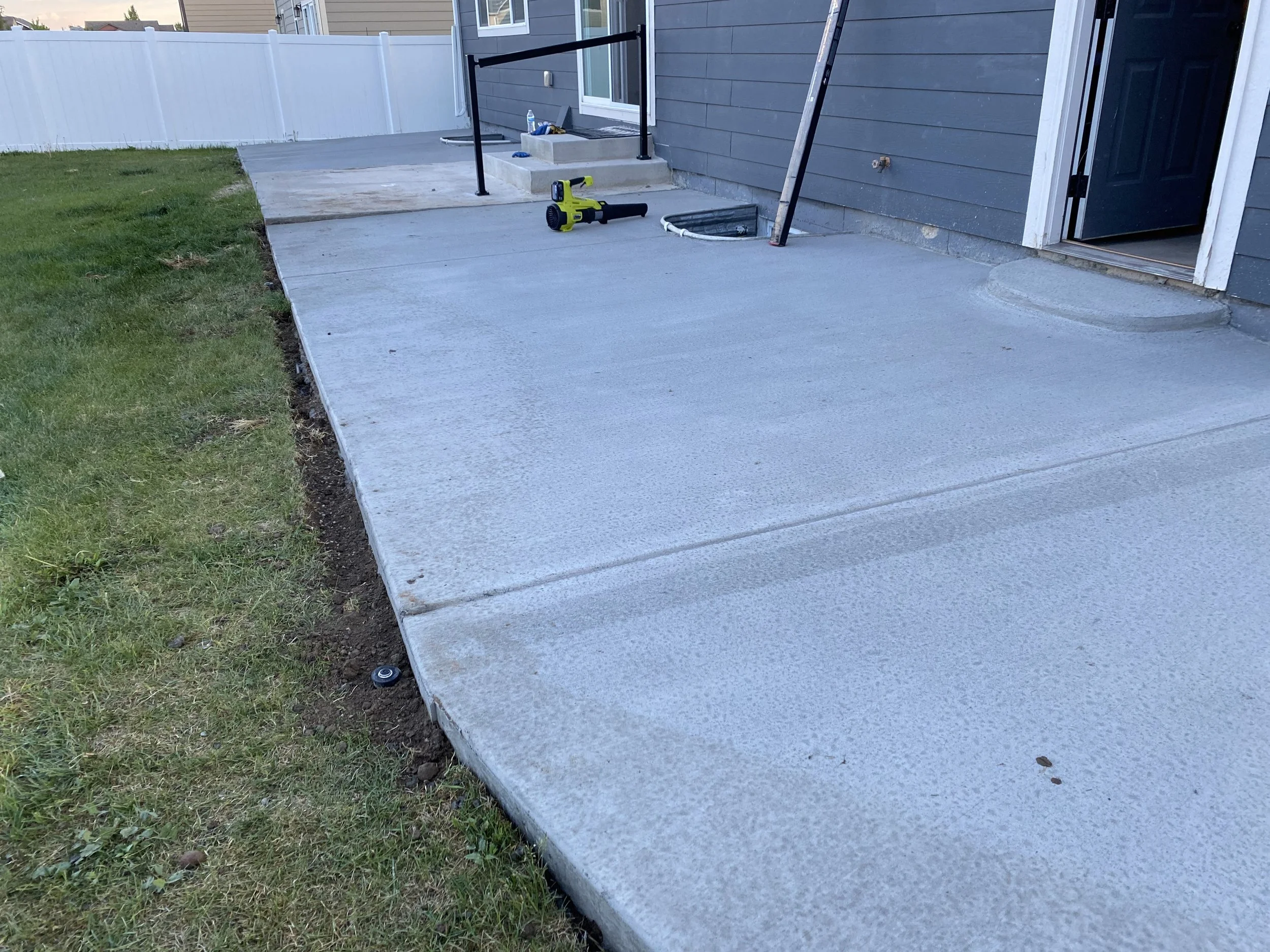 Newly poured concrete patio with construction tools, near a gray house and a white fence.