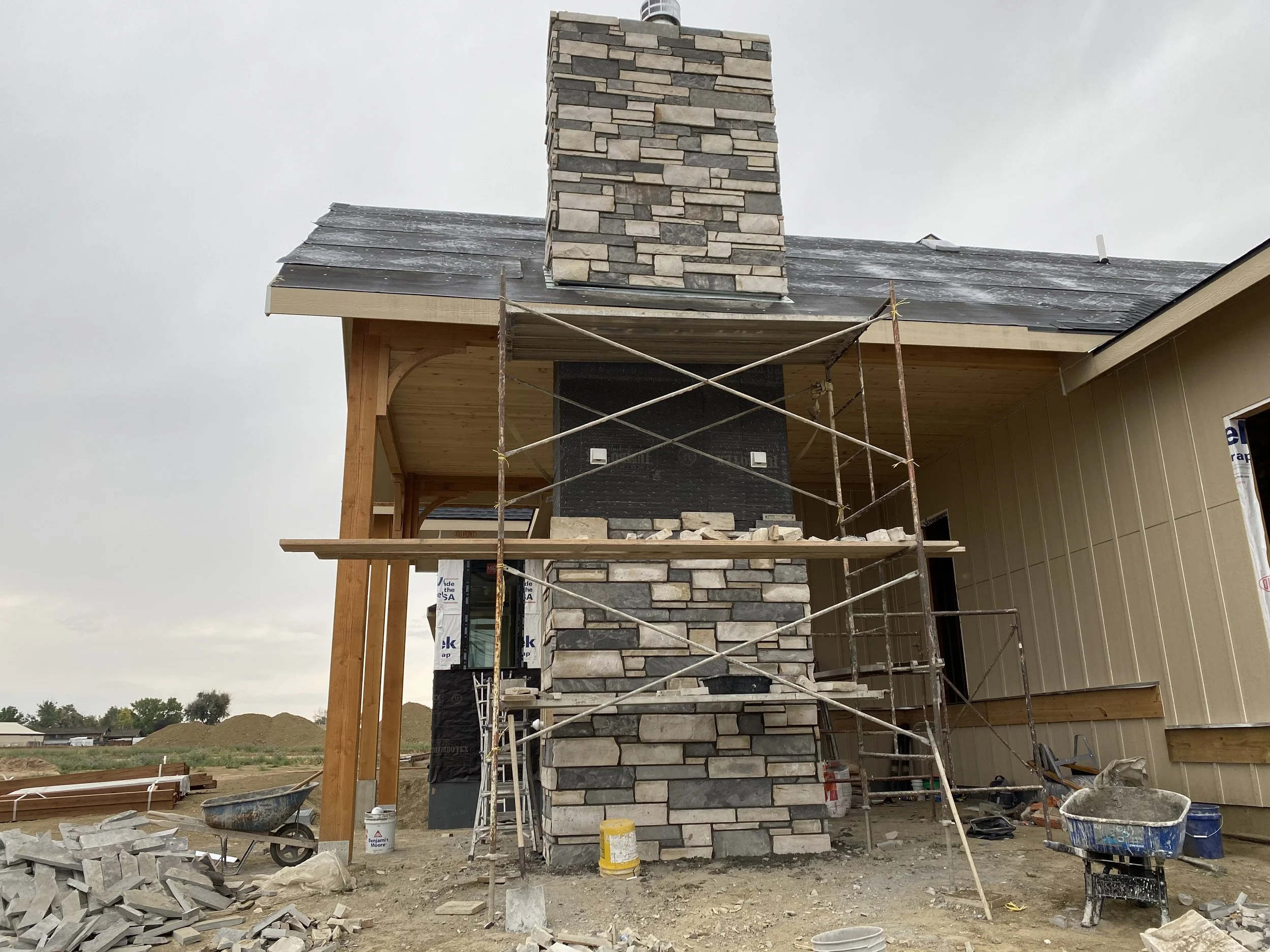 Construction site of a house showing a stone chimney and part of the exterior wall with scaffolding.