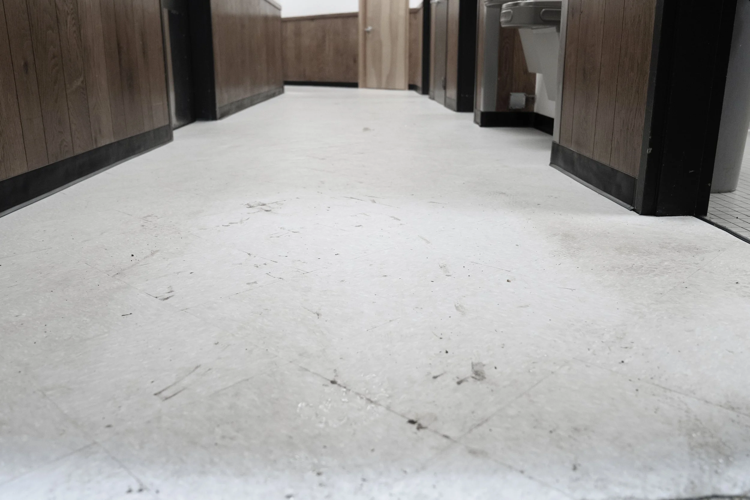 Low-angle view of a corridor with wooden walls, a white floor, and a partially visible paper towel dispenser on the right side.