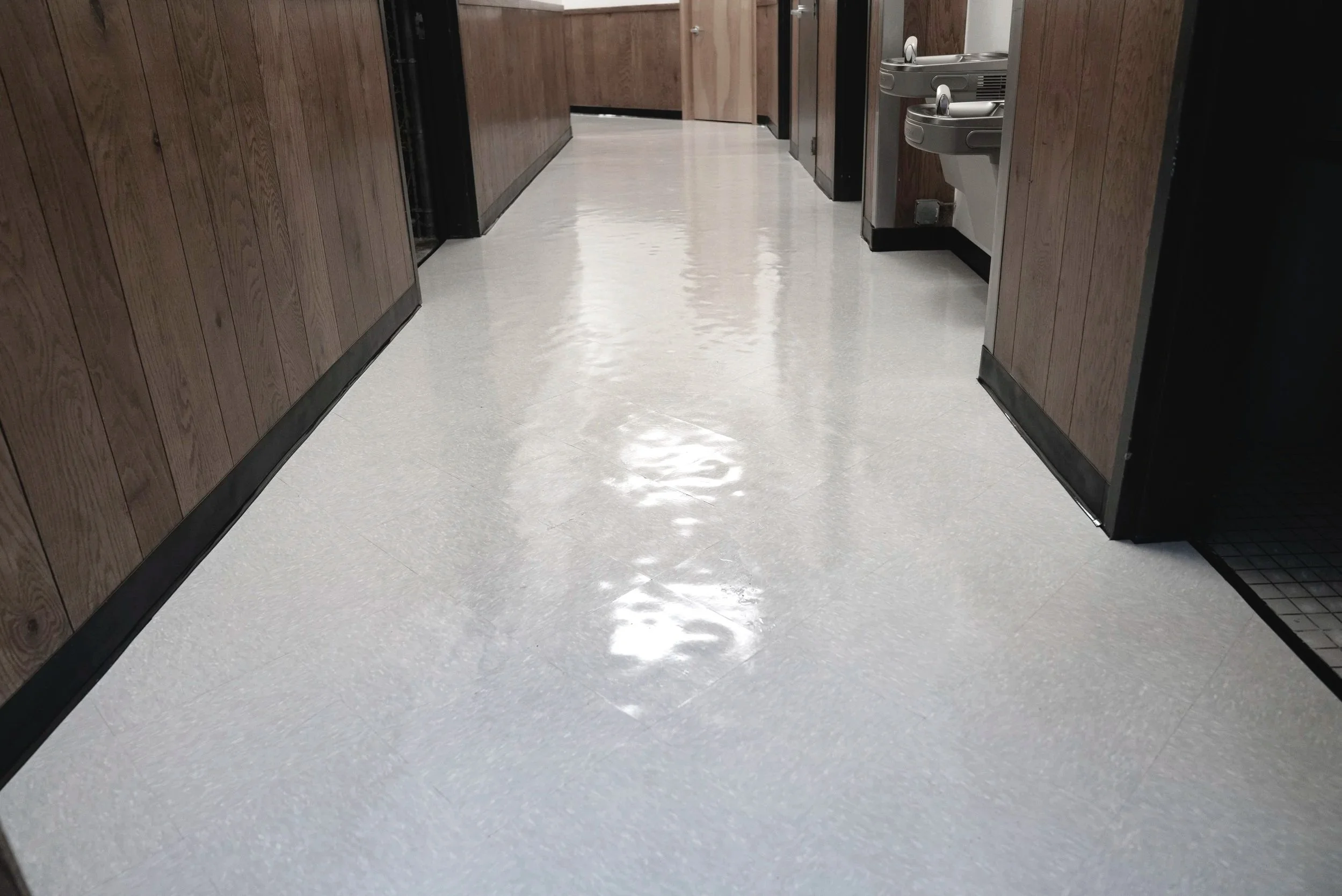 A hallway with wood-paneled walls, a shiny light-colored tile floor, and water fountains on the right side.