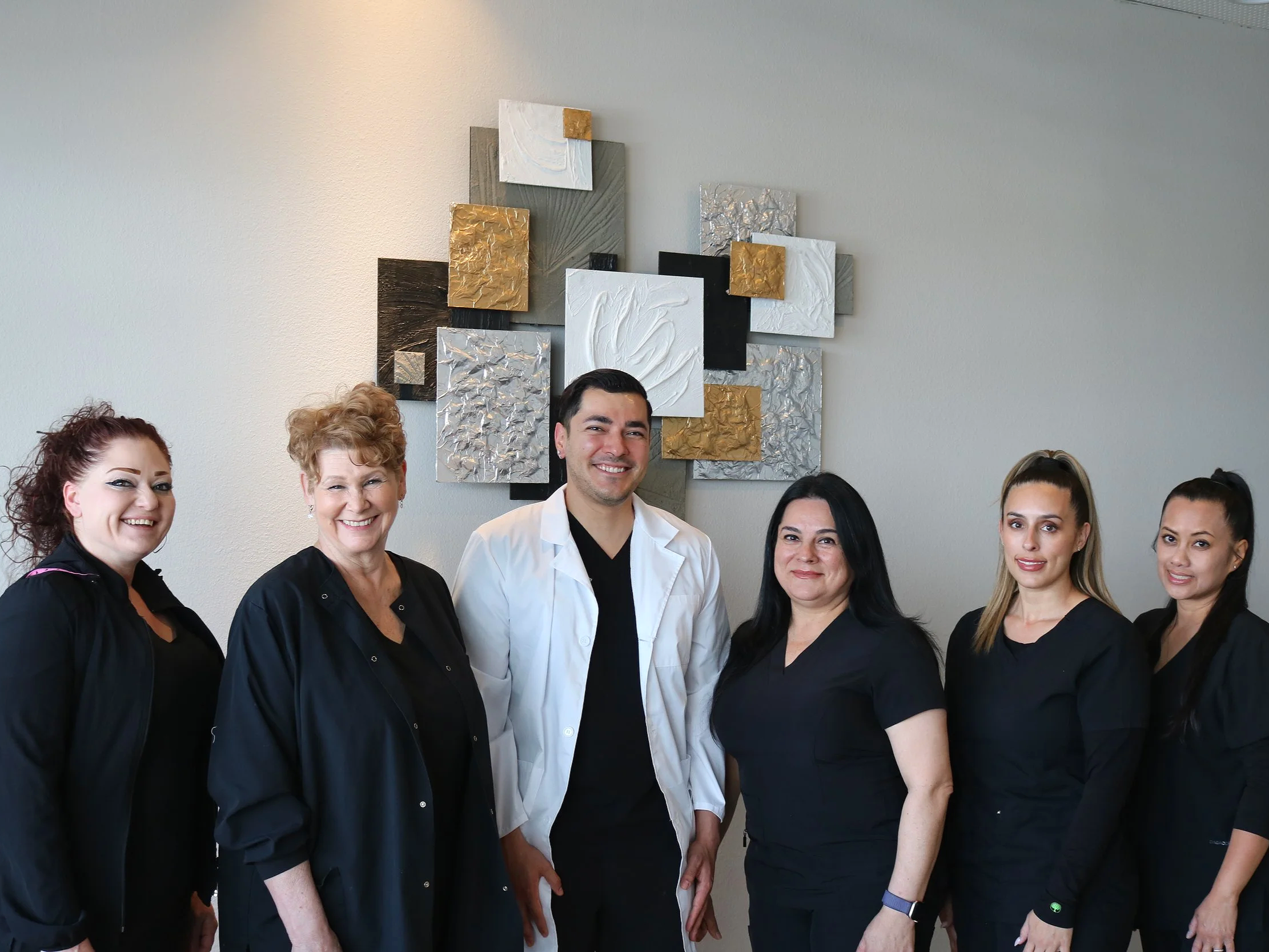 Team group photo of six people standing together indoors, smiling, with abstract wall art behind them.