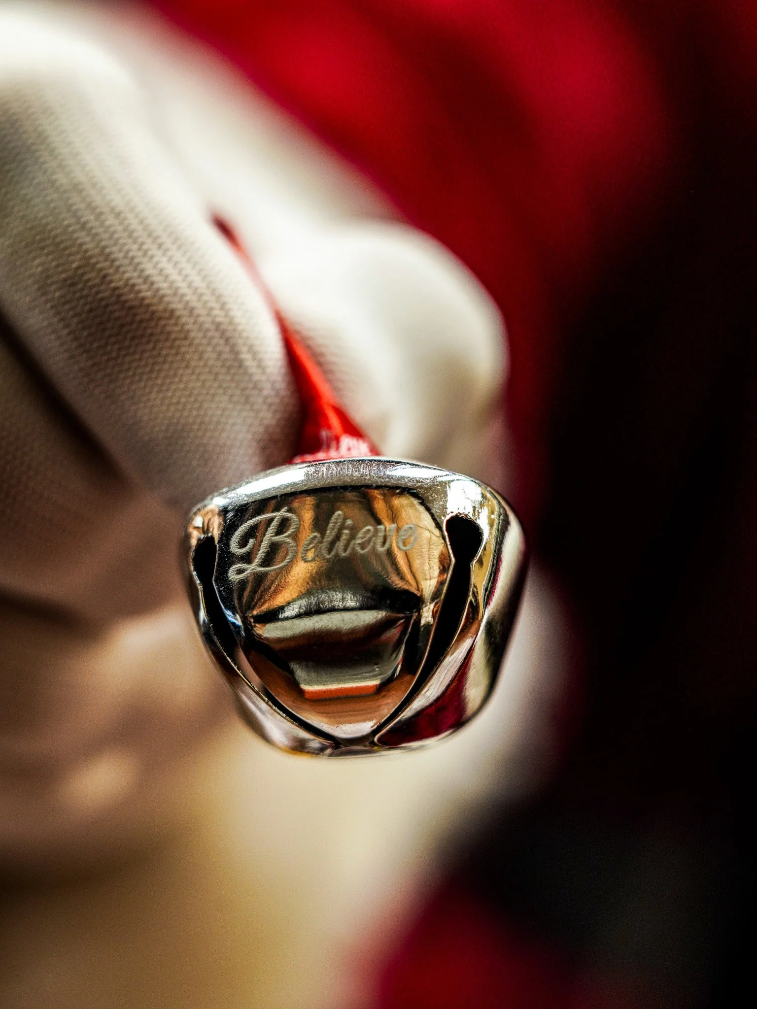 Close-up of a silver ring with the word 'Believe' engraved on it, being held by a hand wearing a white glove.