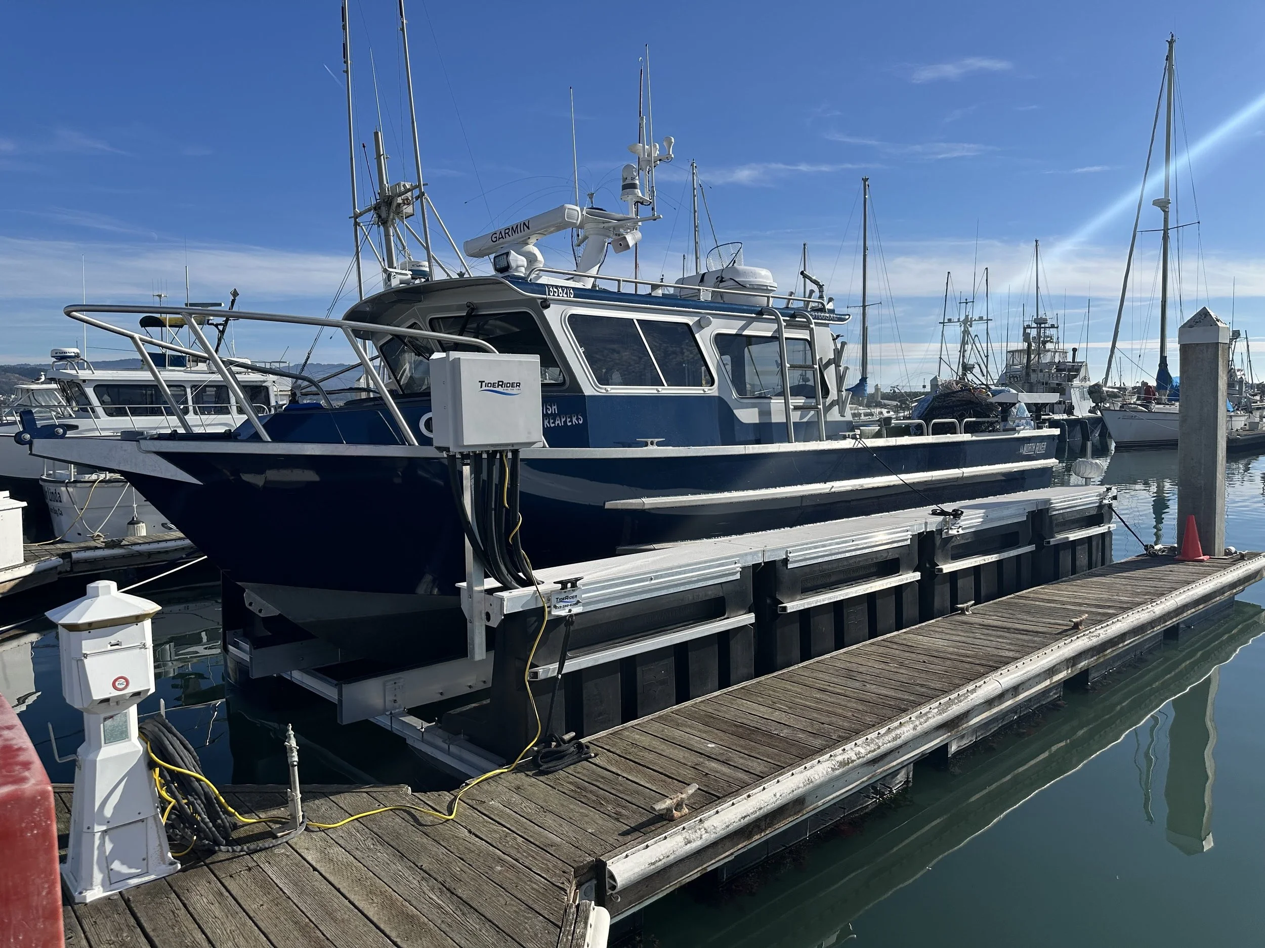 A boat docked at a marina on a sunny day, with several sailboats and yachts in the background.