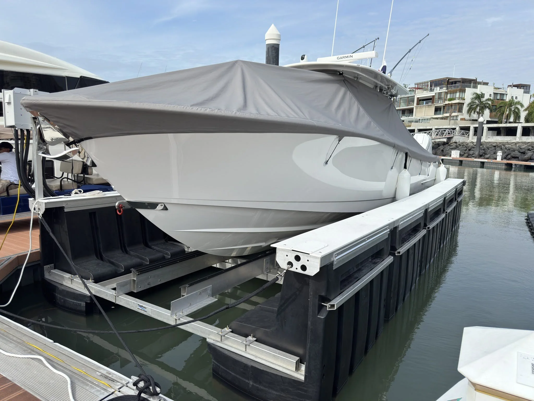 A white yacht docked at a marina with a grey cover over the deck, surrounded by floating black dock sections.