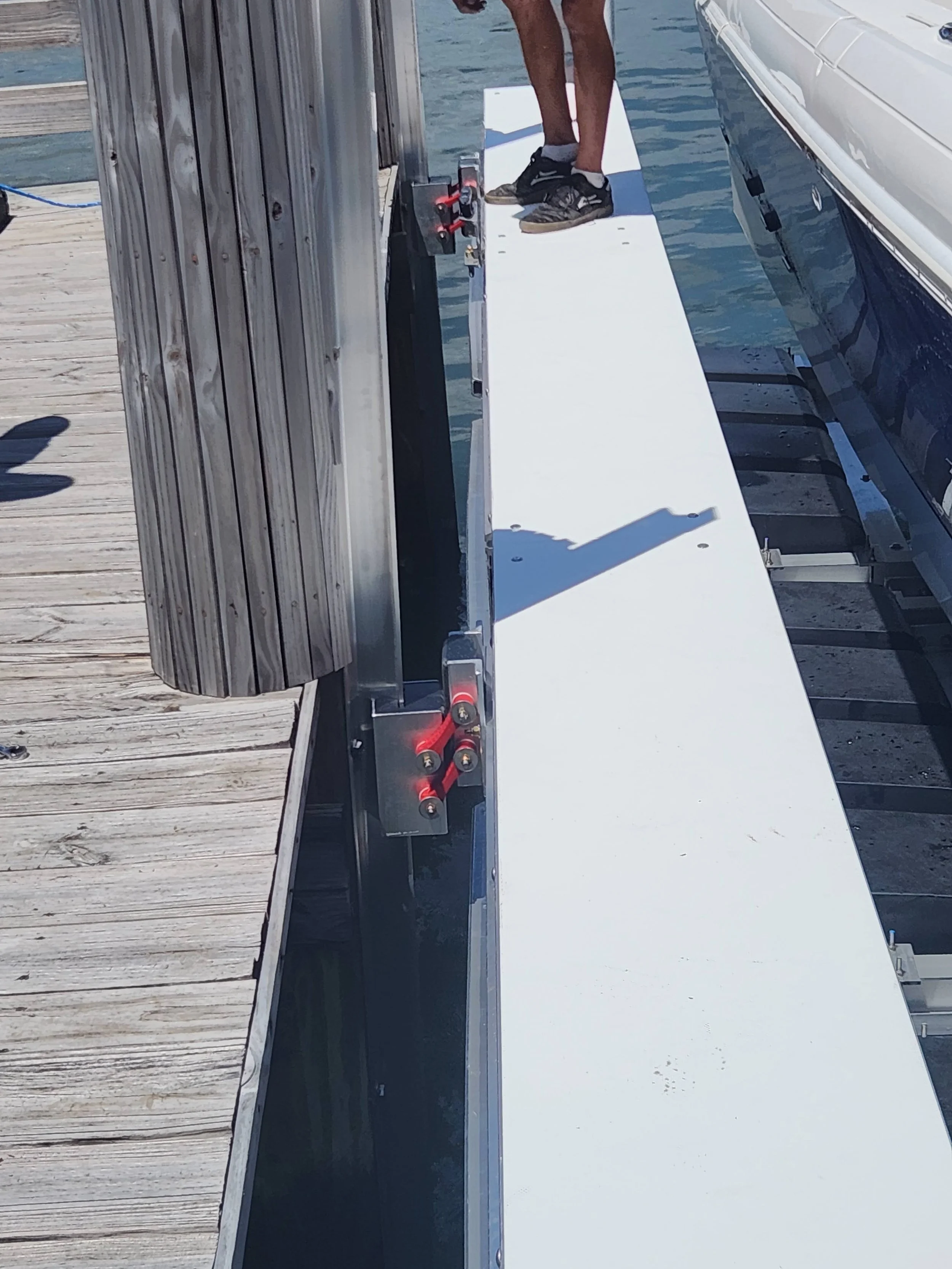 A person standing on a white floating dock at a marina, next to a boat, with a wooden dock on the left side.