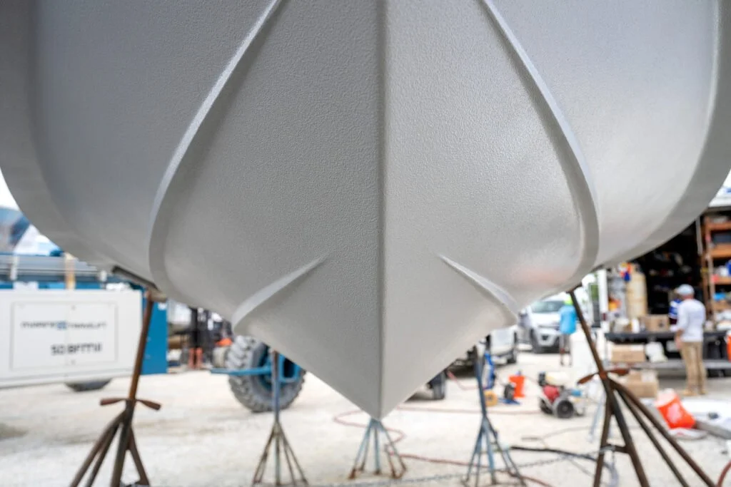 Close-up of the bow of a boat on supports at a boatyard, with tools and people in the background.