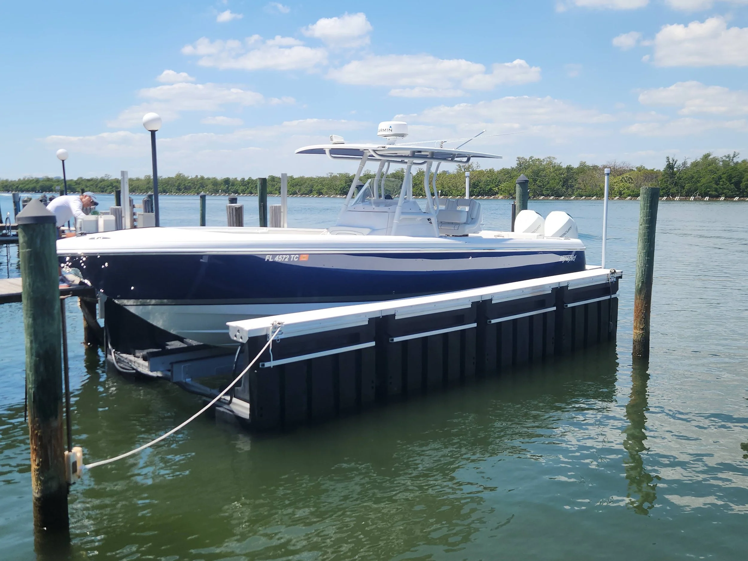 A blue and white motorboat docked at a marina with calm water, wooden posts, and lamp posts, under a partly cloudy sky.