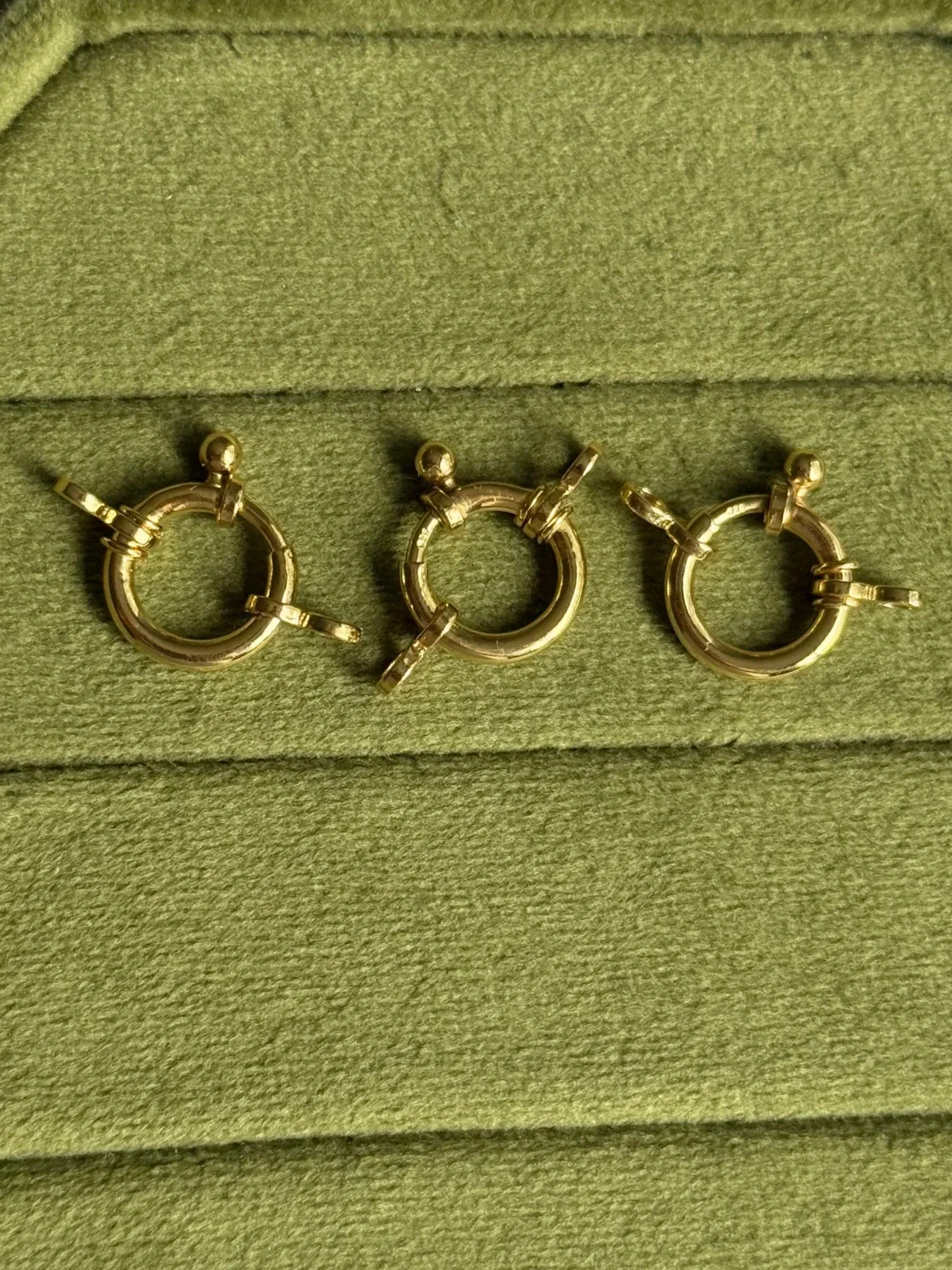 Three gold hoop earrings with latch clasps on a green textured background.