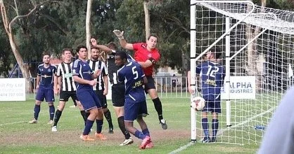 Soccer players on the field with the goalkeeper catching the ball near the goal post.