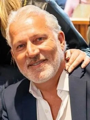 A middle-aged man with short gray hair and a beard, wearing a black button-up shirt, smiling while looking at the camera.