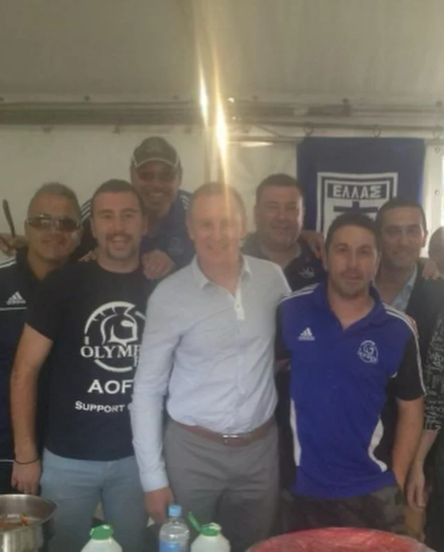 Group of men posing together inside a tent with sports banners in the background.