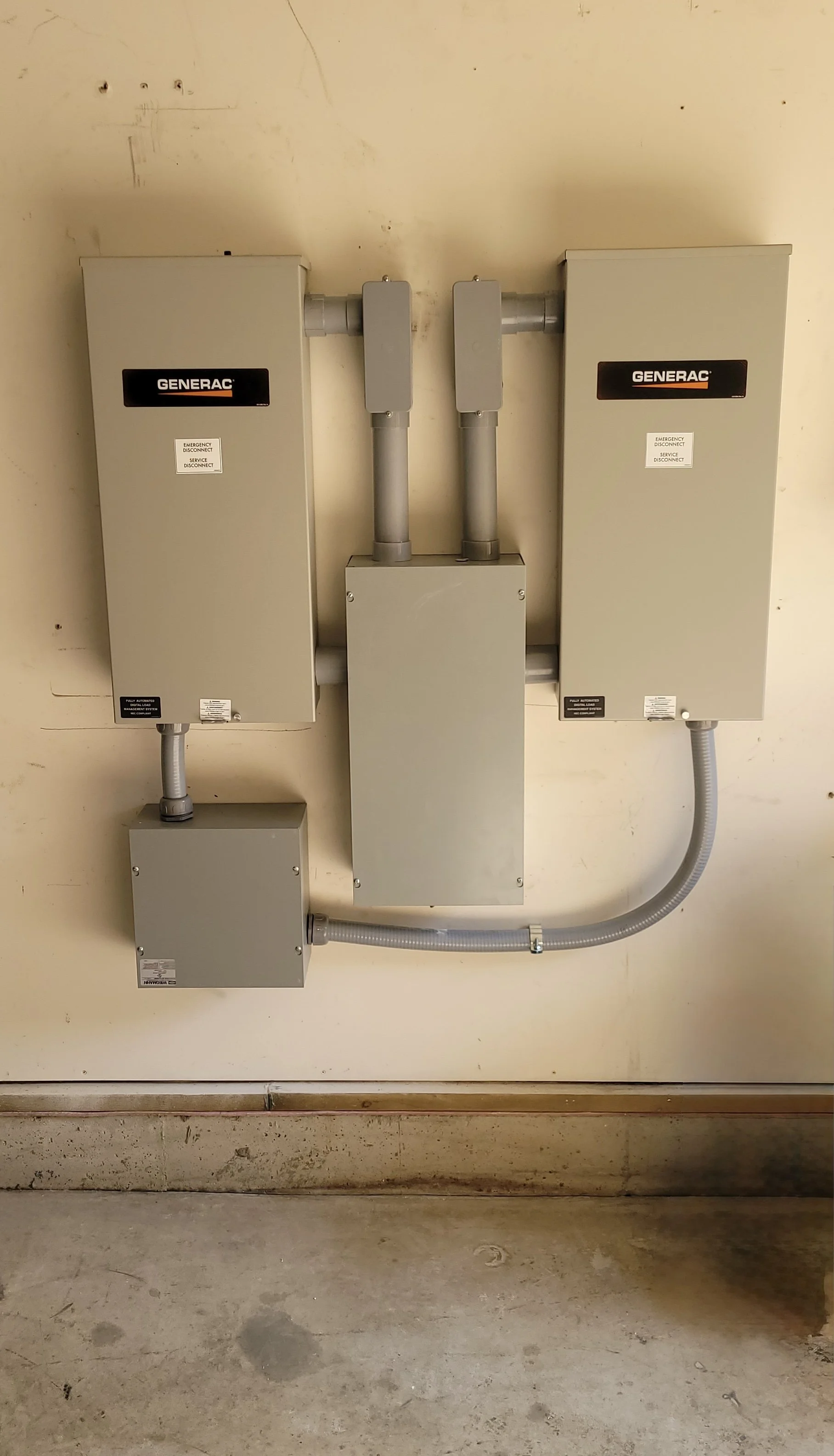 Electrical boxes and conduits on a beige wall in a utility room with a concrete floor.