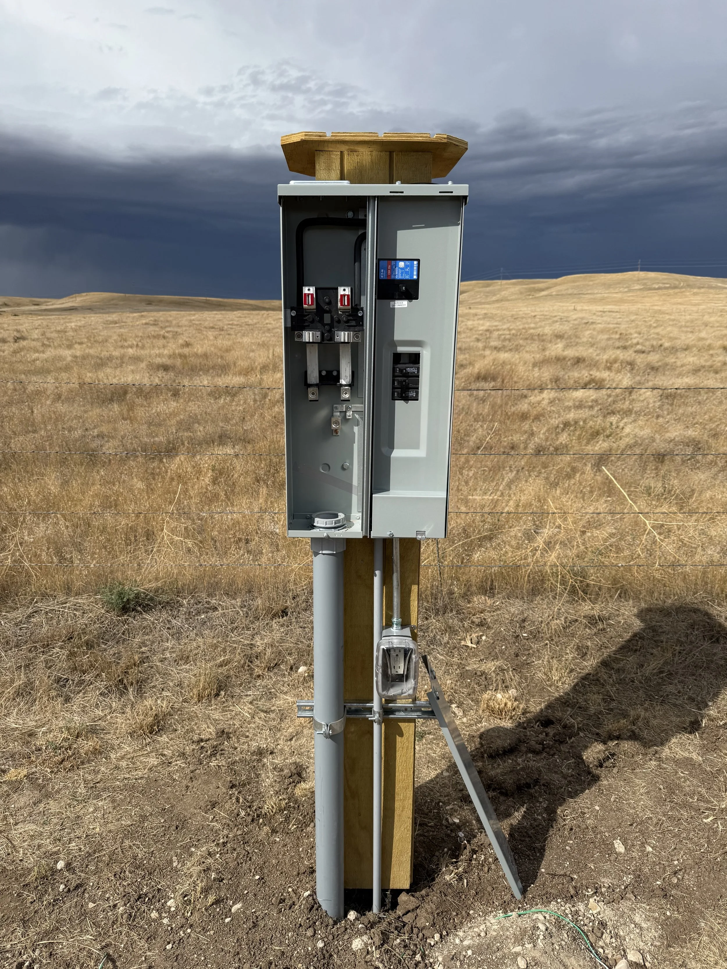 A weather station mounted on a wooden post in a dry, grassy field with storm clouds in the background.