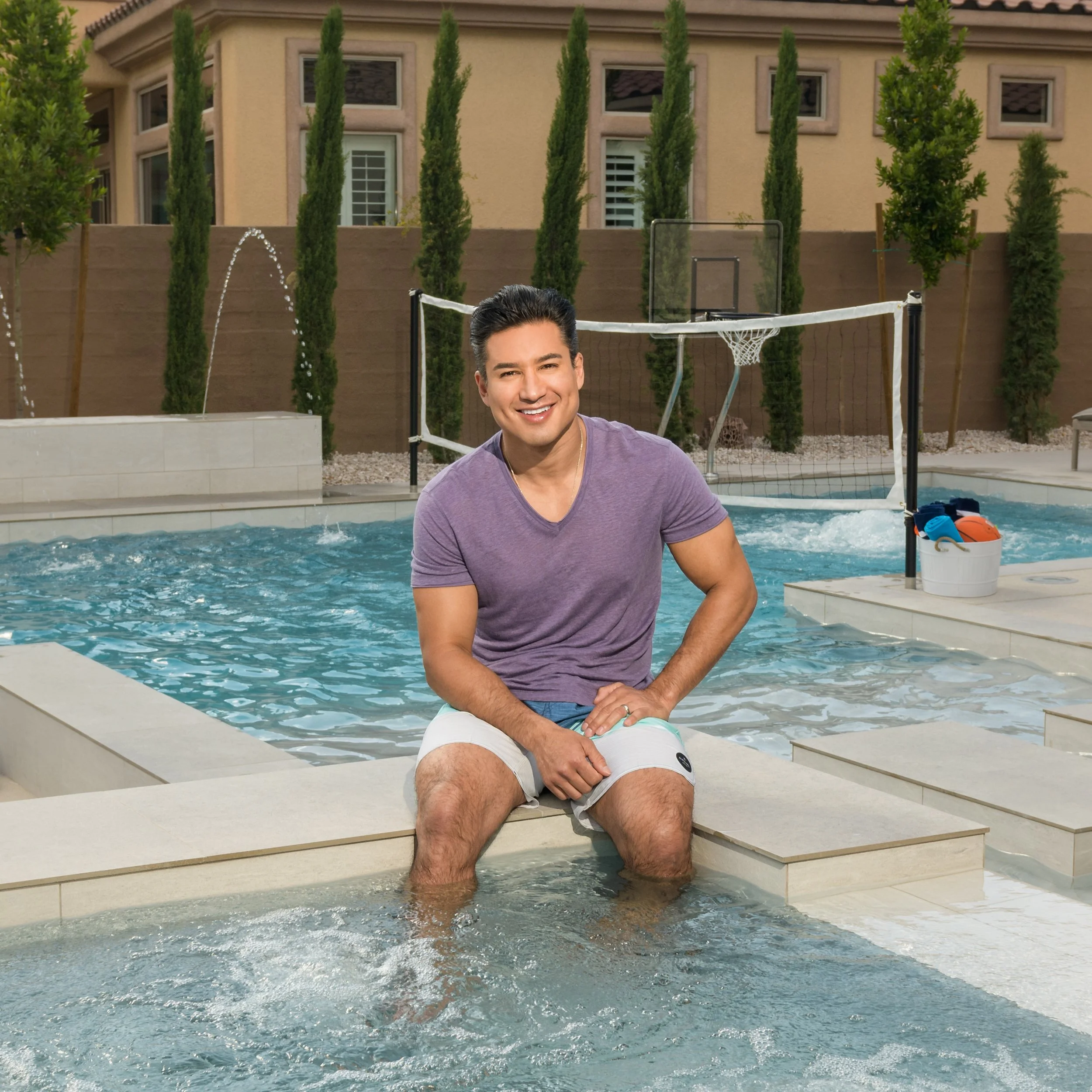 Smiling man sitting on the edge of a swimming pool with his feet in the water.
