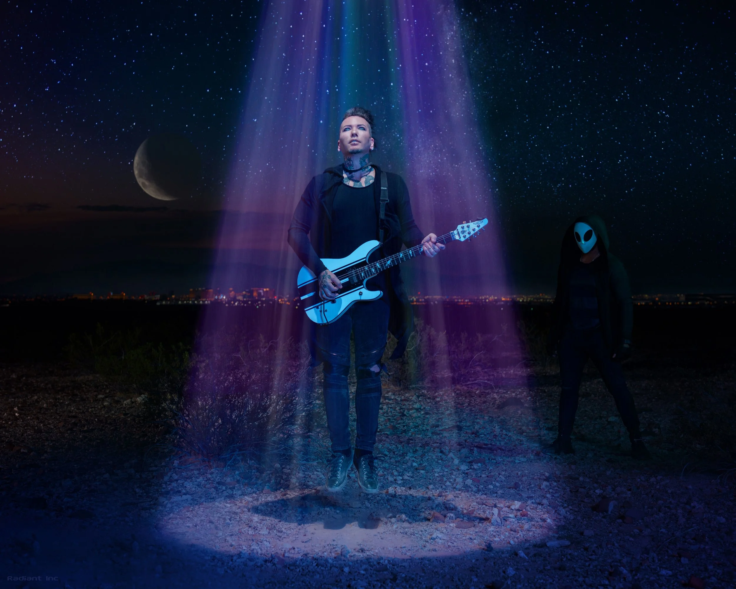 A person jumping with a guitar illuminated by colorful light beams in a starry night landscape with city lights and a moon, and another person wearing an alien mask standing nearby.