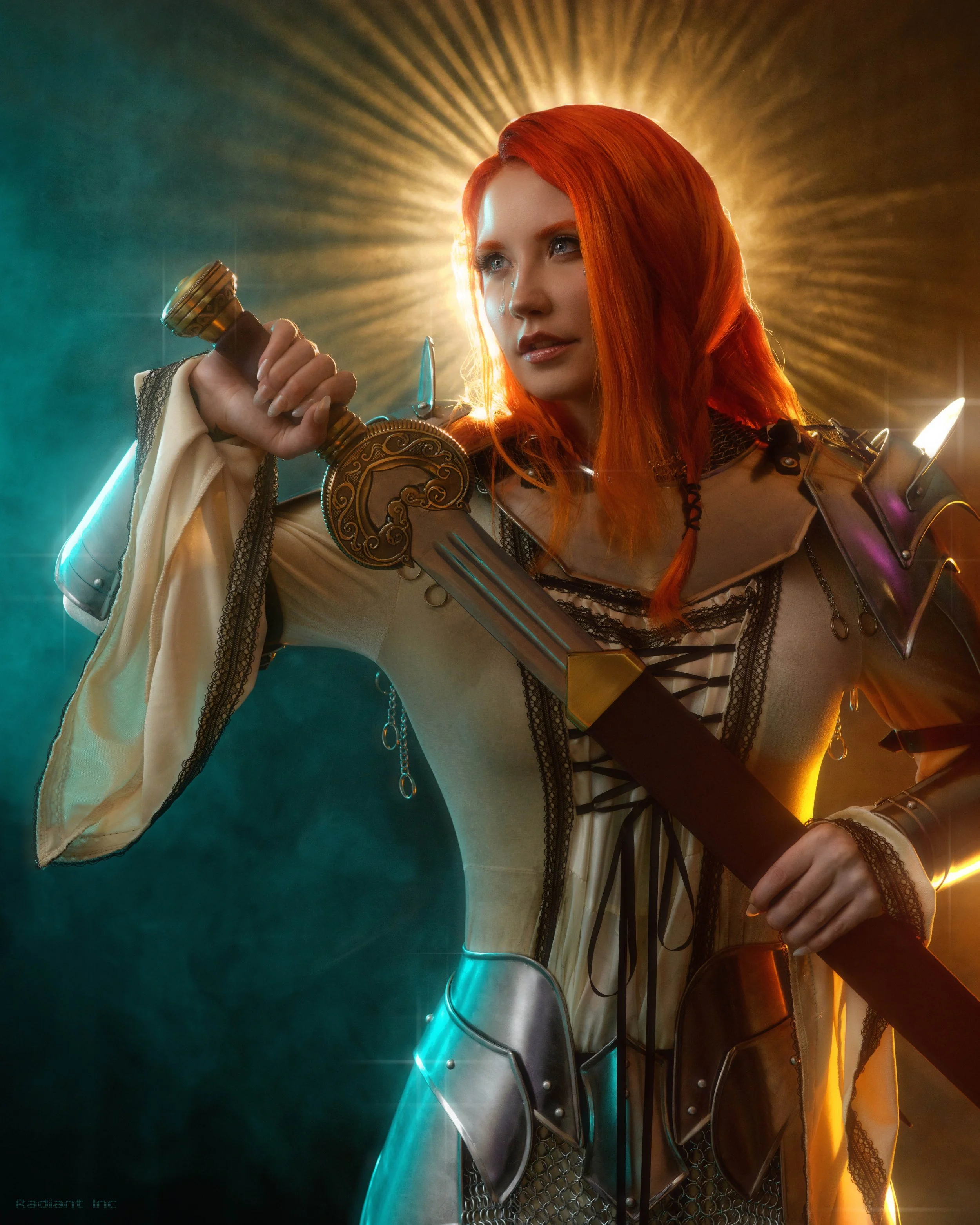A woman dressed as a fantasy warrior with red hair holding a sword, illuminated by a radiant halo behind her.