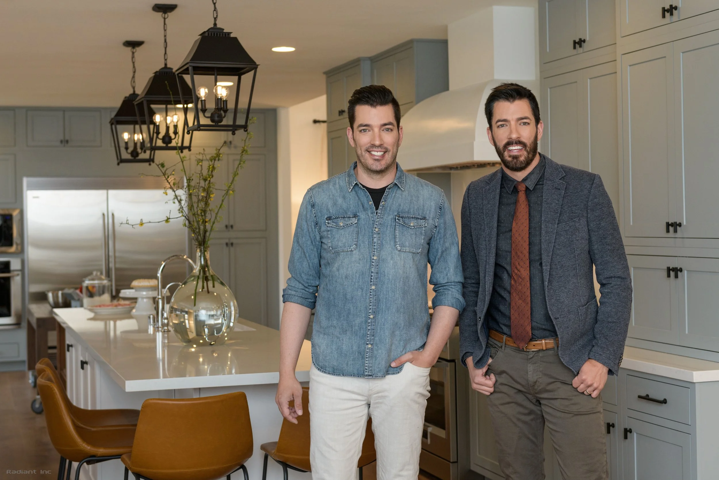 Two men standing in a modern kitchen, smiling at the camera.