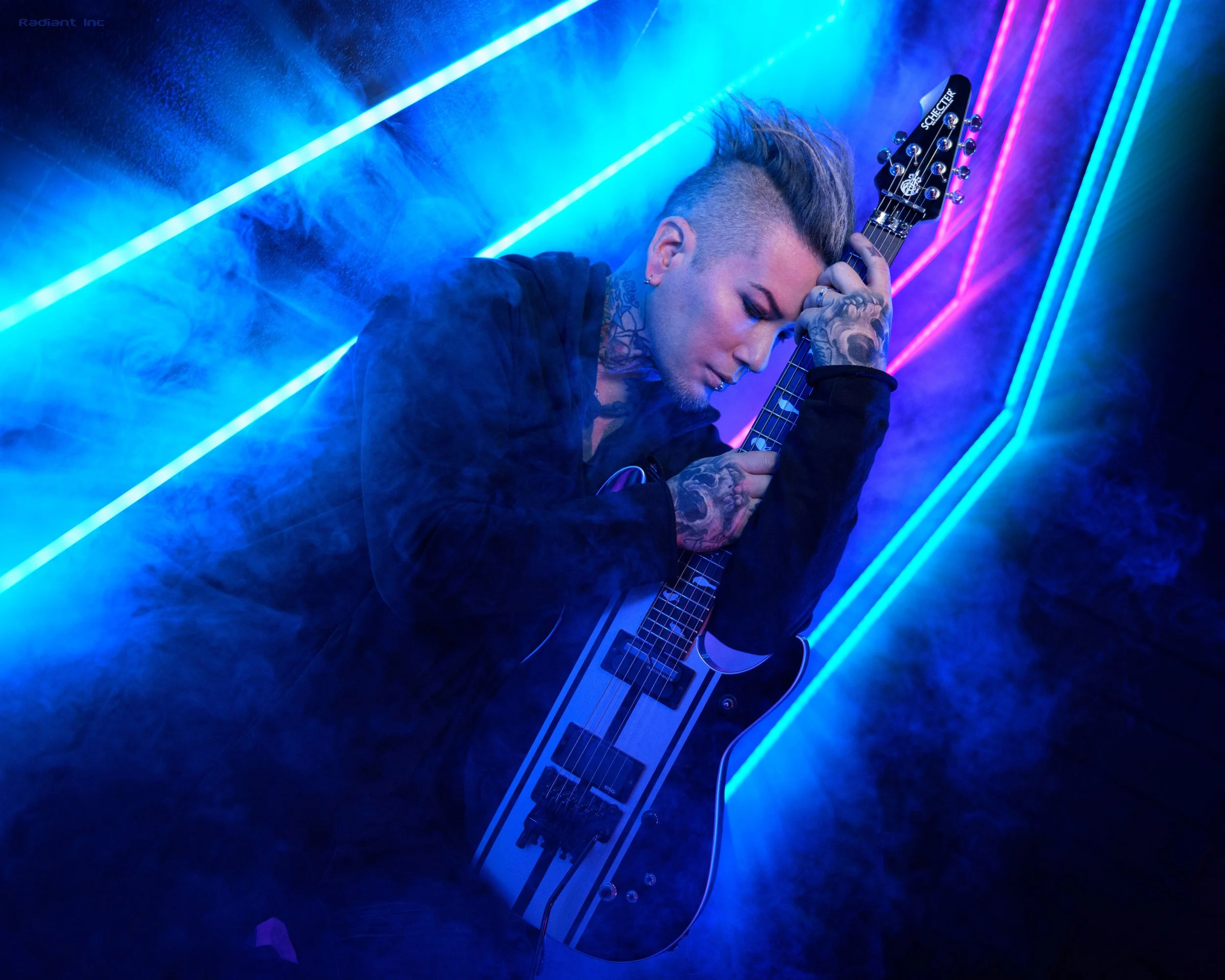 A person with tattoos and a mohawk hairstyle, holding and leaning on a black and white electric guitar, surrounded by blue and purple neon lights and fog.