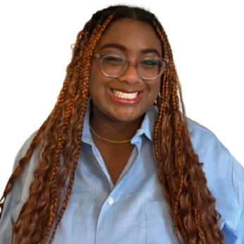 A smiling woman with long, curly, reddish-brown hair, glasses, and wearing a light blue button-up shirt.