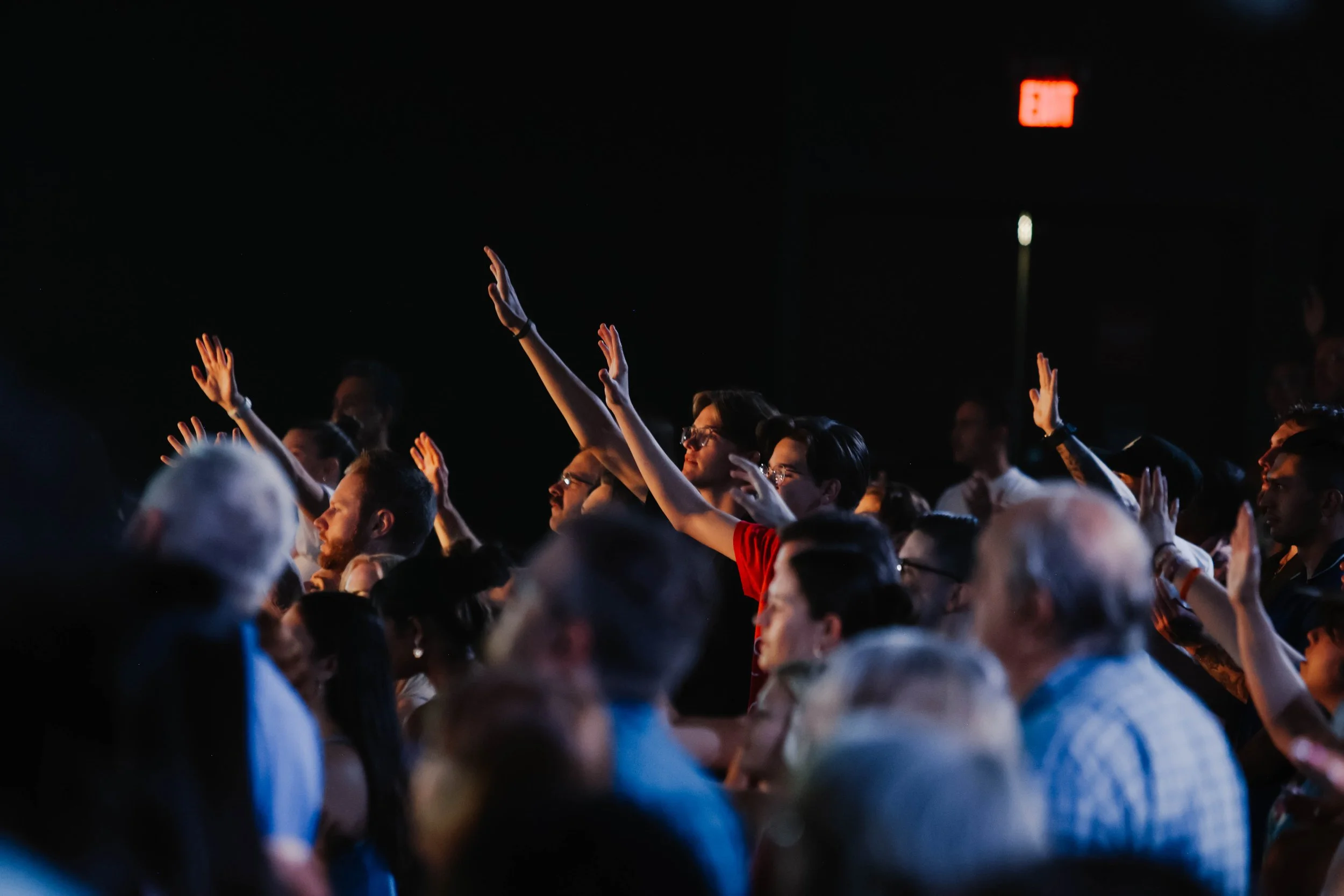 A family of three, a woman, a man, and a young boy, smiling and posing together indoors, with a colorful abstract mural in the background.
