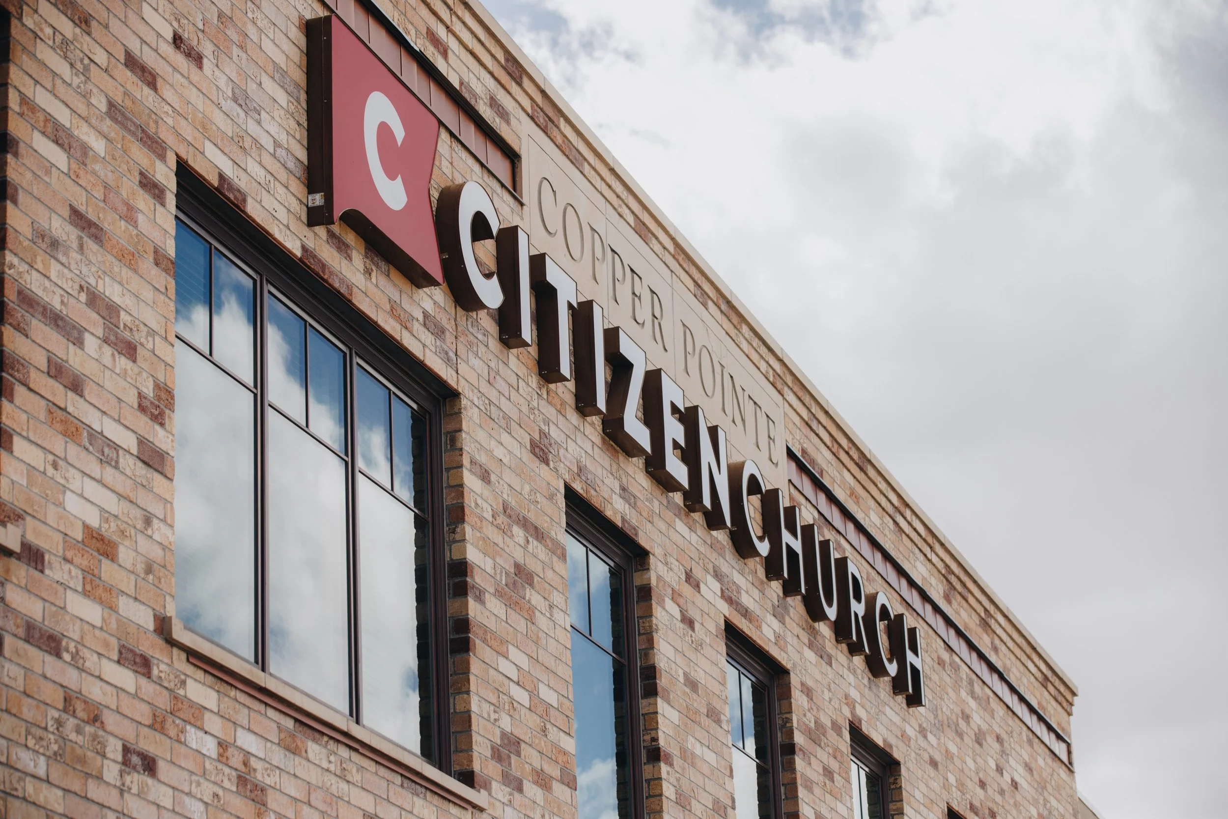 Brick building with sign reading "Copper Pointe Citizen Lounge" and logo with a red background and a white circle and red dot inside