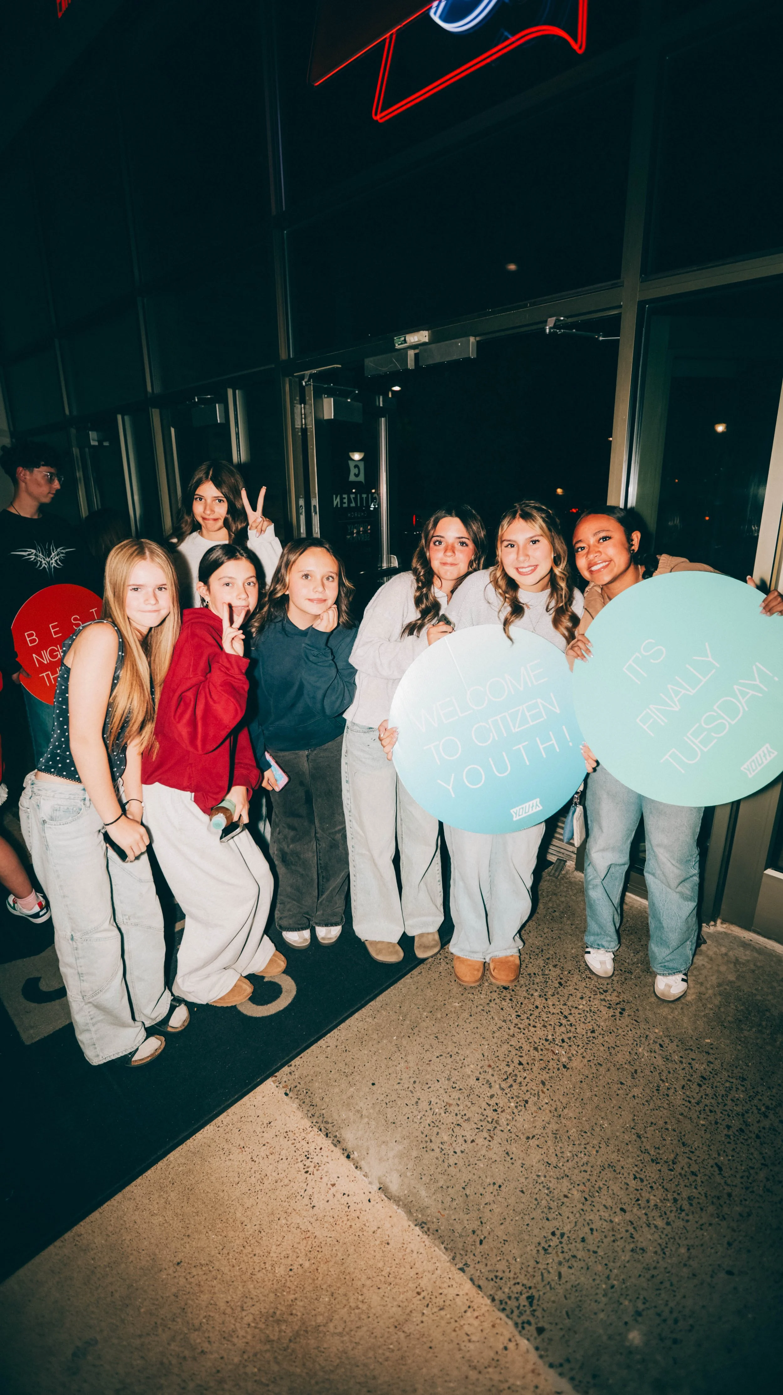 Group of young people holding signs celebrating youth event at night.