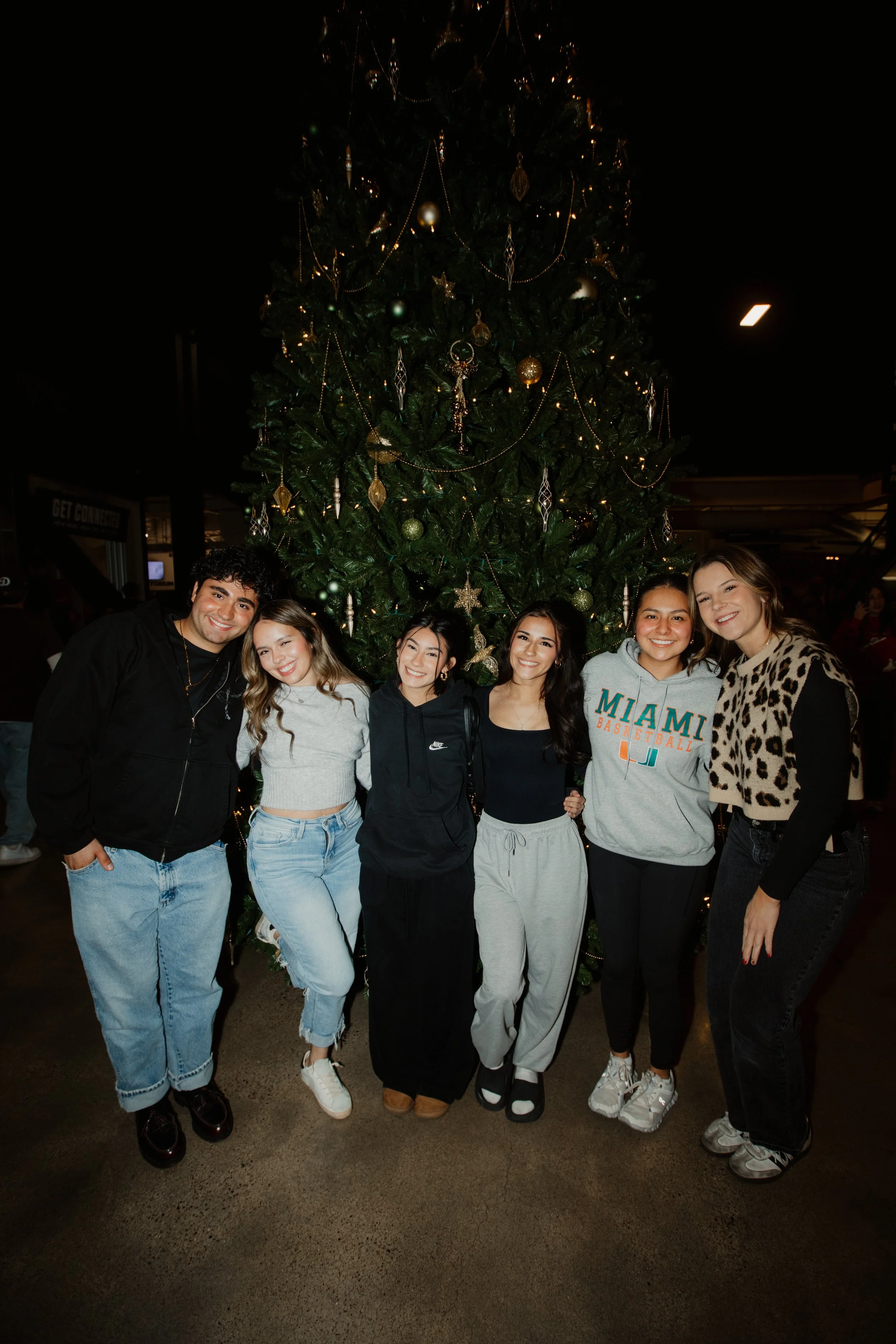 Six young people standing in front of a decorated Christmas tree, smiling for the camera.