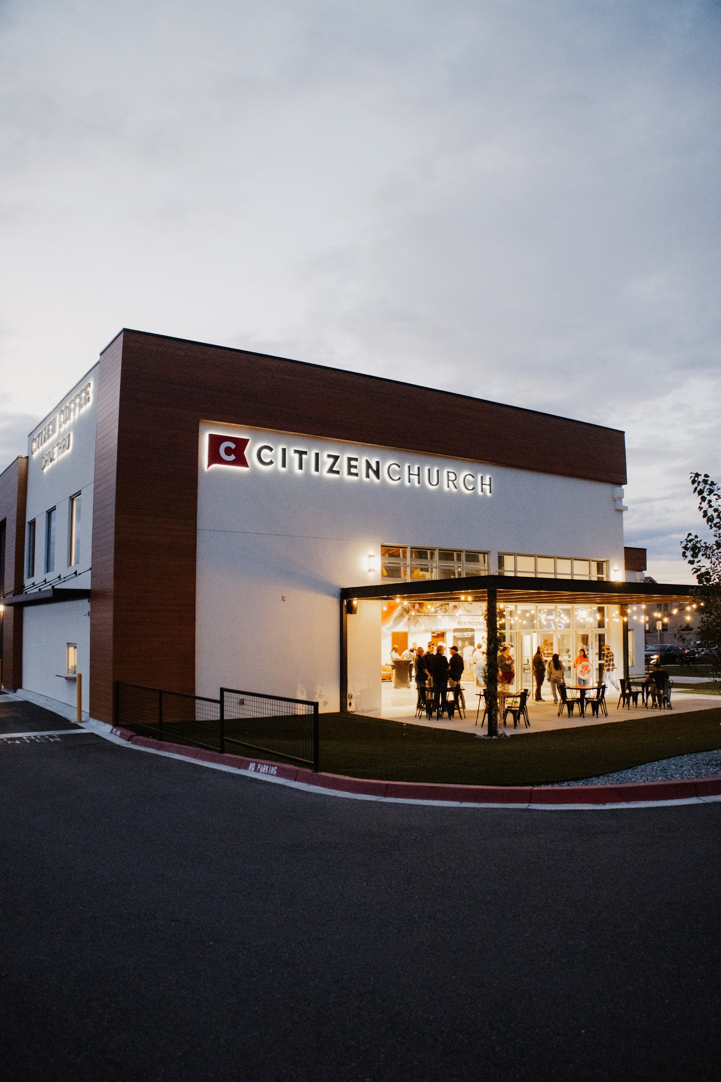 Exterior of Citizen Church building at dusk with people gathering outside, string lights, and illuminated signage.